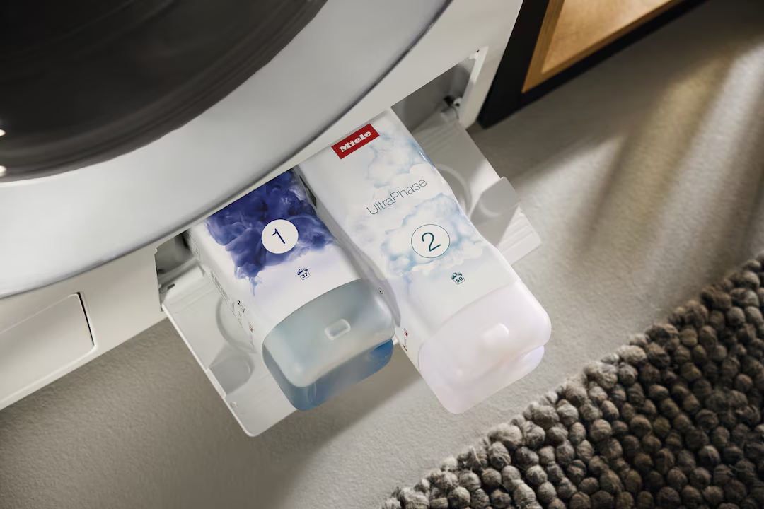 Due capsule di detersivo Miele, 1 e 2, in una lavatrice.