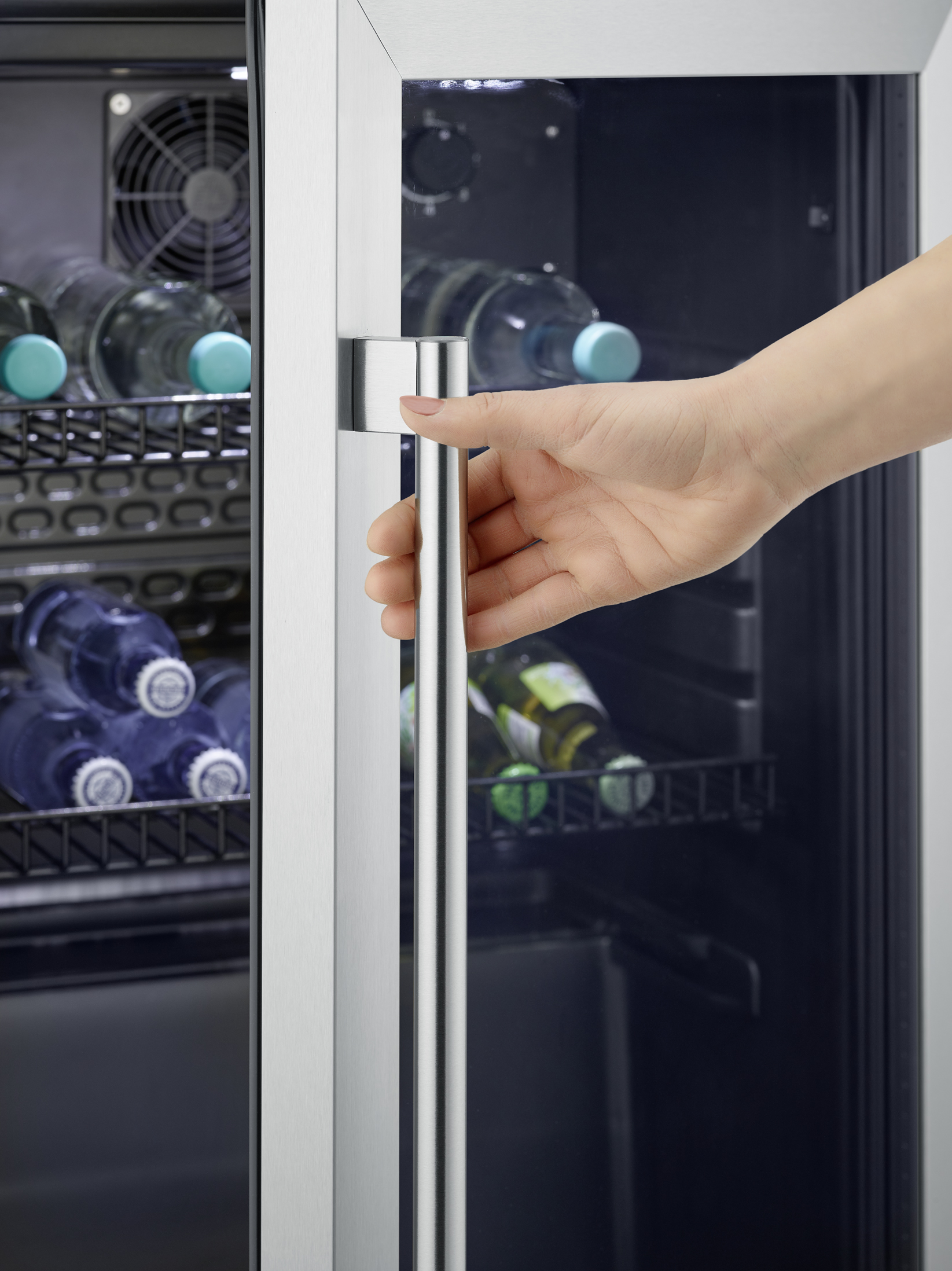 Hand öffnet Kühlschranktür mit Glasfront, gefüllt mit Flaschen.