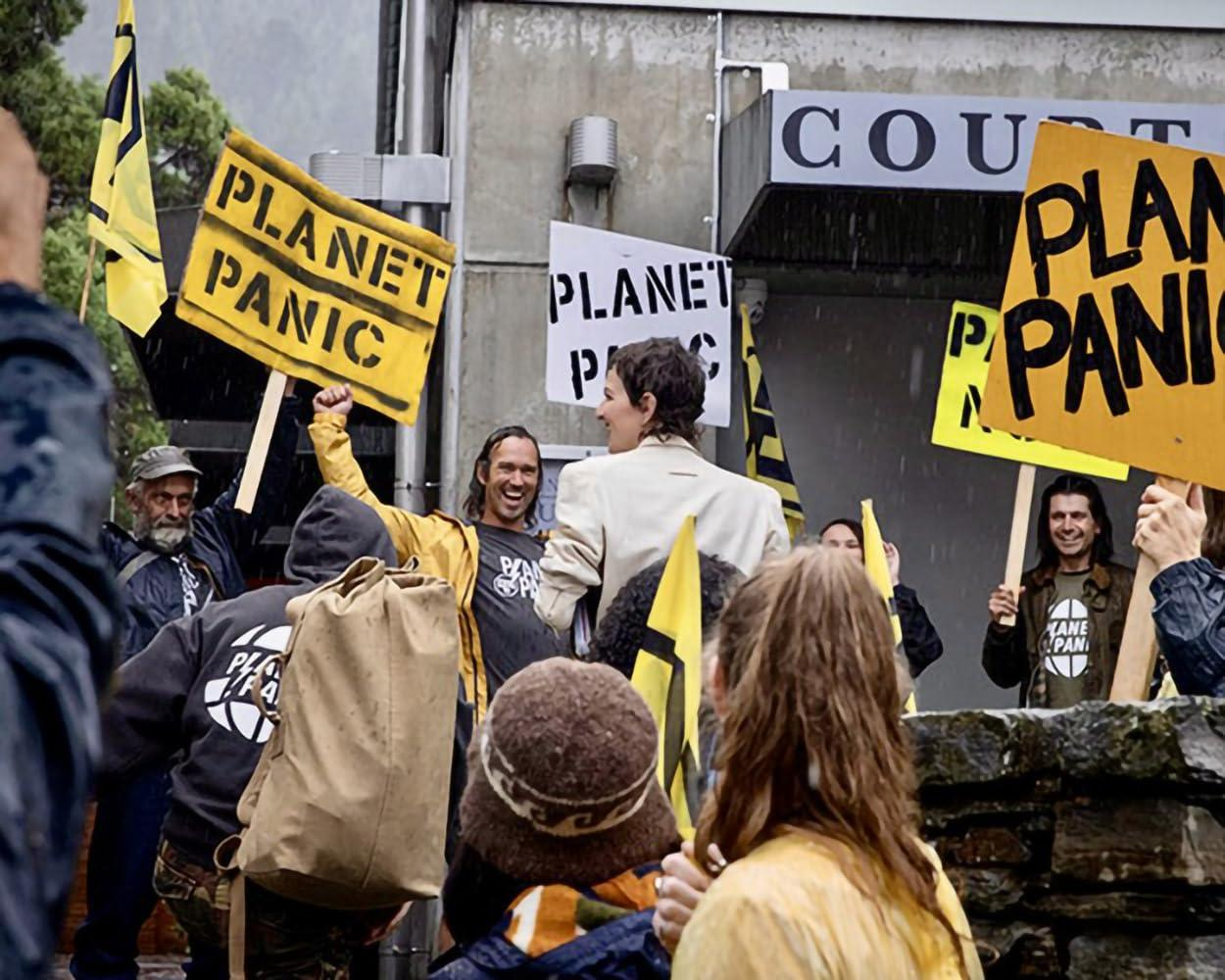 Demonstranten halten Schilder mit der Aufschrift „PLANET PANIC“ vor einem Gerichtsgebäude.
