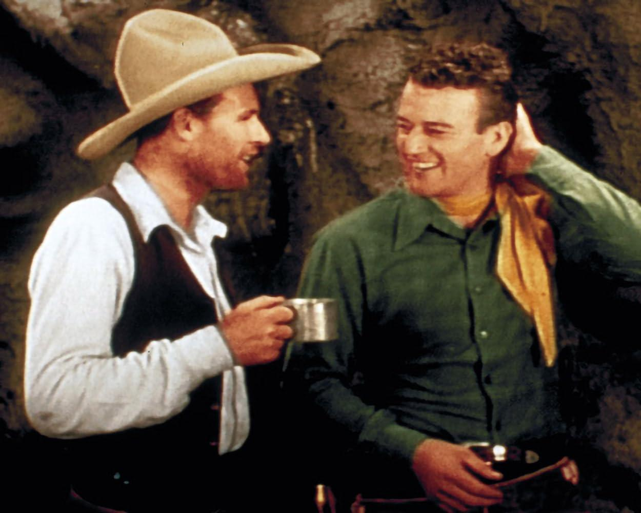 Zwei Männer in Westernkleidung unterhalten sich. Einer trägt einen Hut und hält eine Tasse.