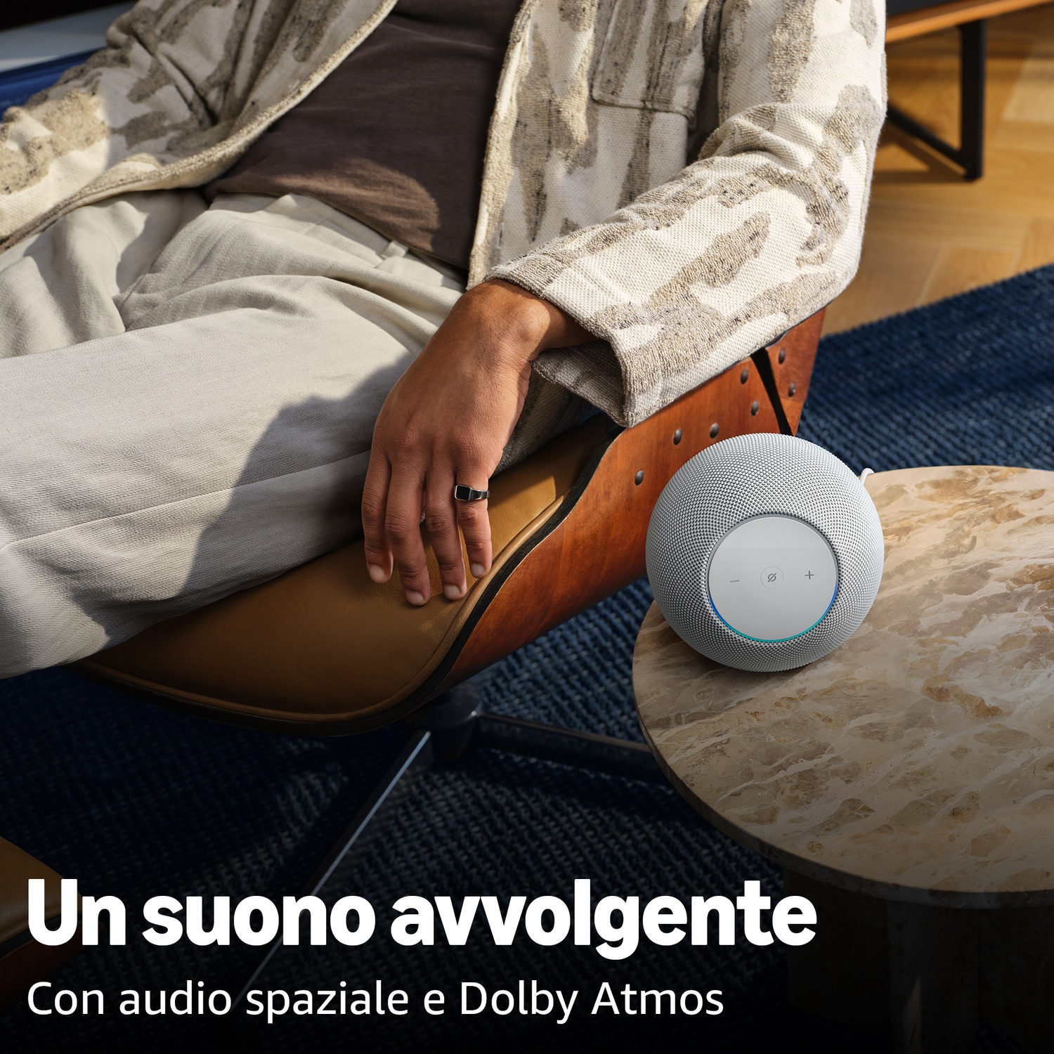 Un uomo siede su una poltrona accanto a un altoparlante rotondo su un tavolino di marmo.