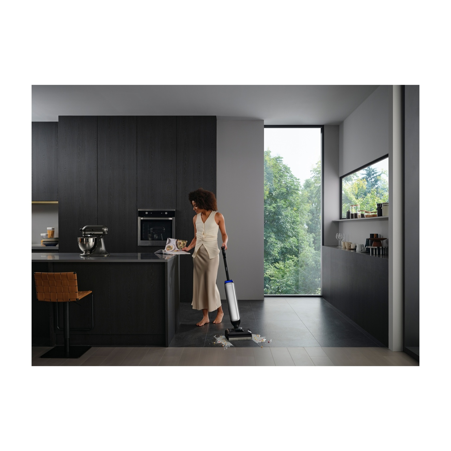 Una donna pulisce una macchia in una cucina moderna con un aspirapolvere bagnato/asciutto.