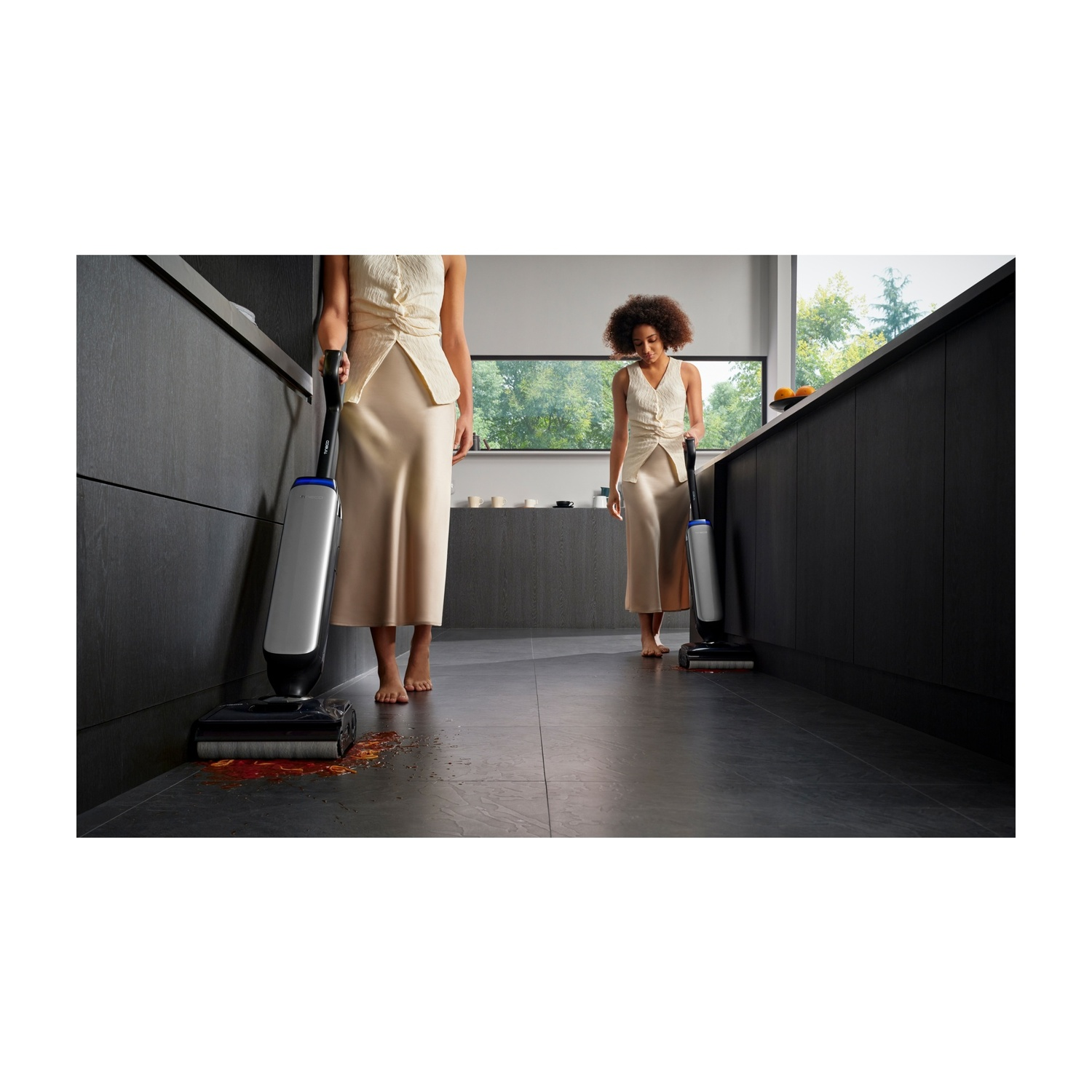 Due donne puliscono un pavimento di cucina versato con aspirapolvere liquidi/solidi.