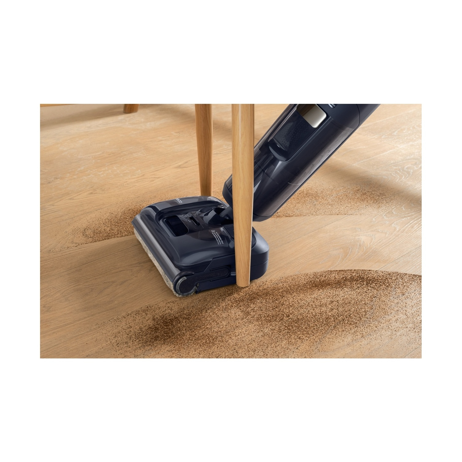 Aspirapolvere blu scuro pulisce polvere marrone da pavimento in legno.