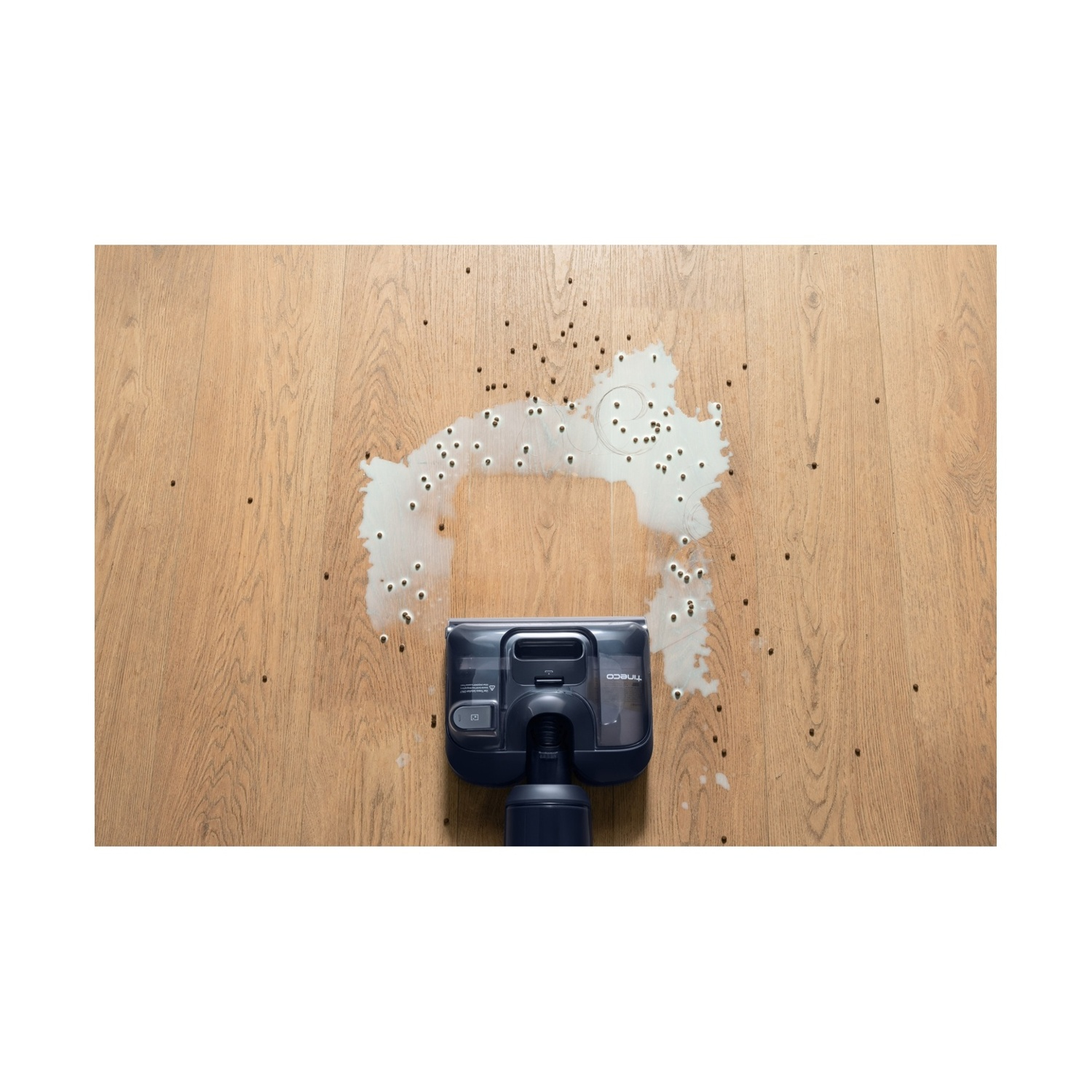 Un aspirapolvere pulisce un pavimento in legno da liquidi versati e detriti.