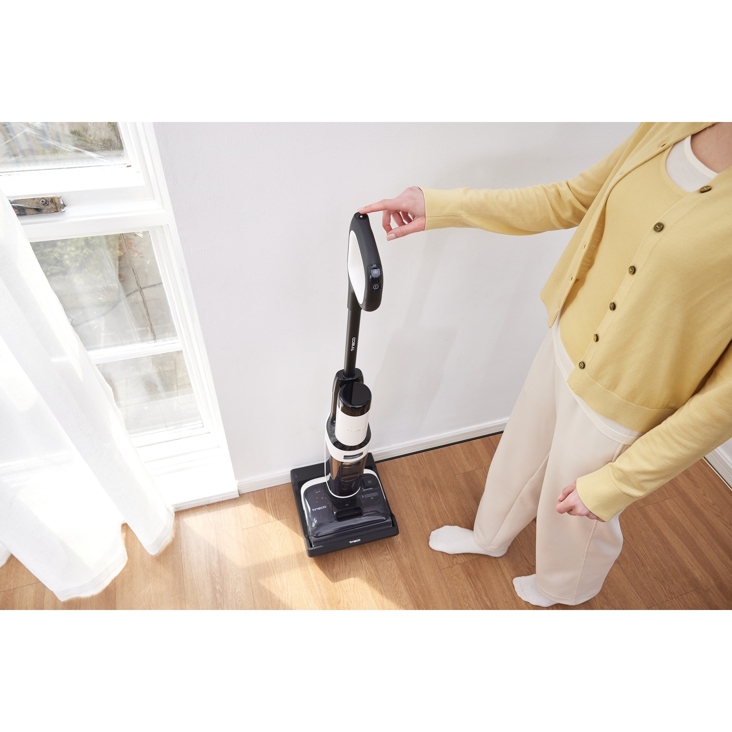 Una persona con cardigan giallo aziona un pulitore per pavimenti bianco e nero.