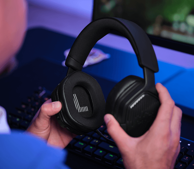 Fekete gamer fejhallgatót tartanak kézben egy billentyűzet fölött.