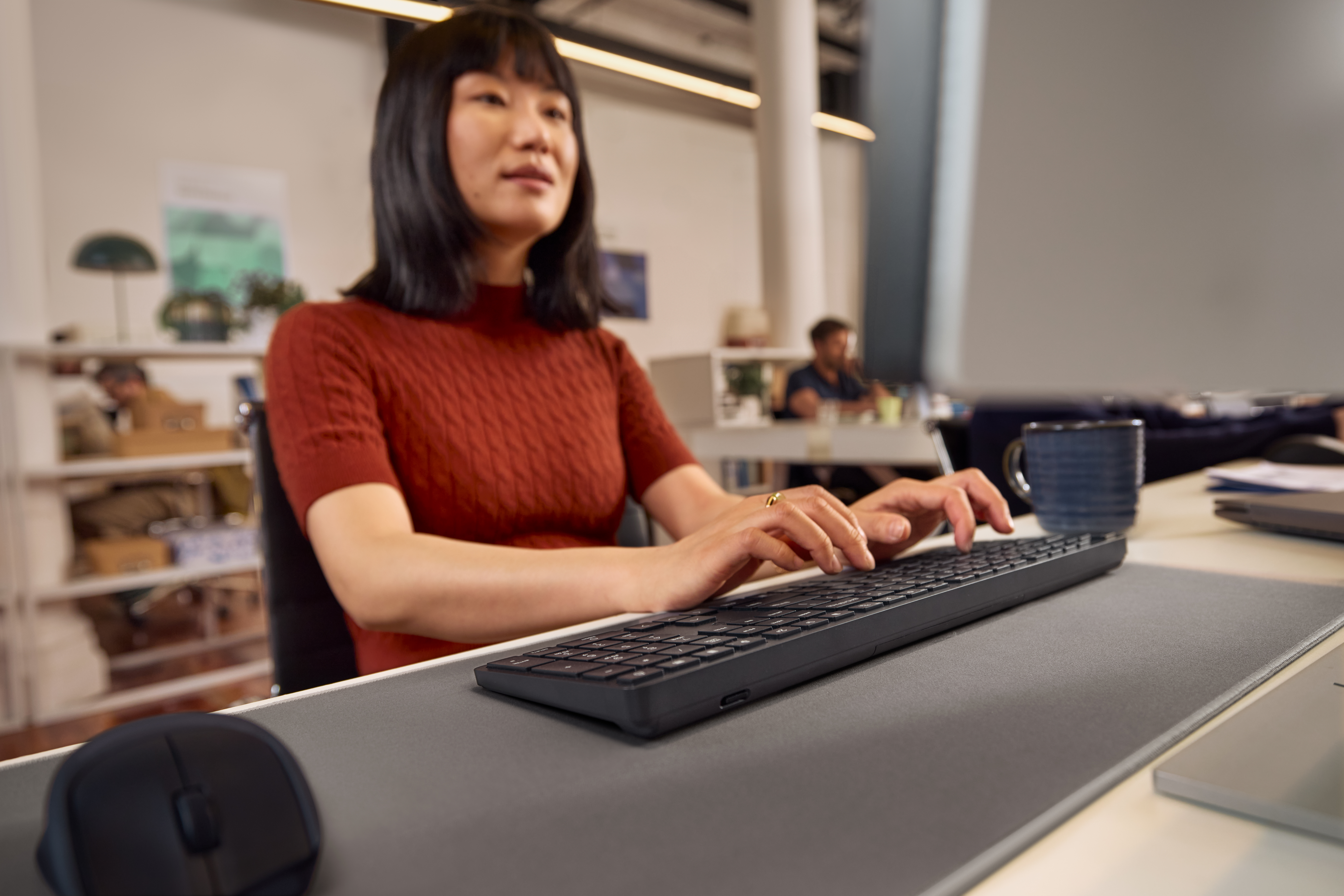 Eine Frau tippt auf einer Tastatur in einem Büro. Eine Maus liegt links.
