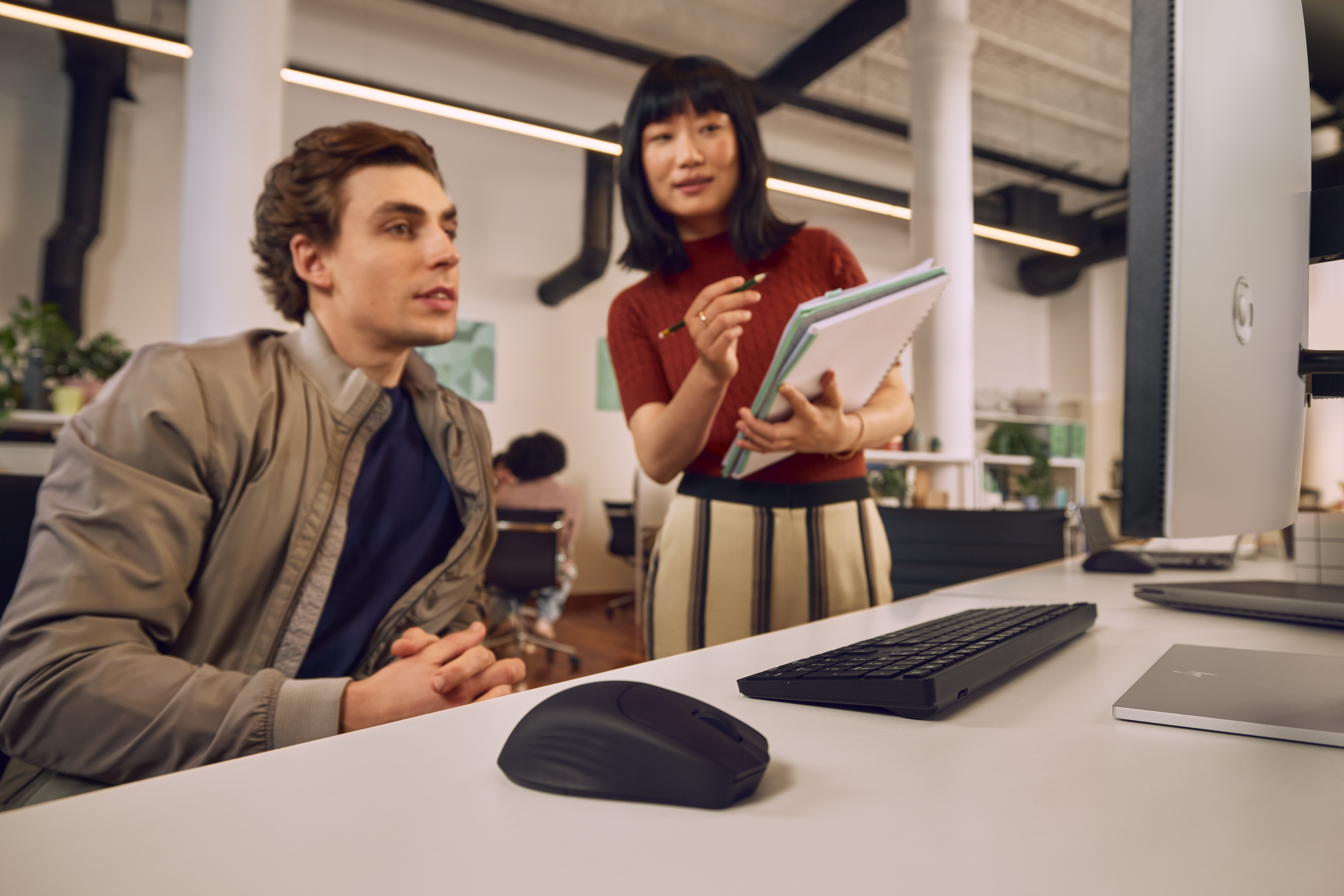 Mann und Frau im Büro besprechen Notizbuch vor Computermonitor.