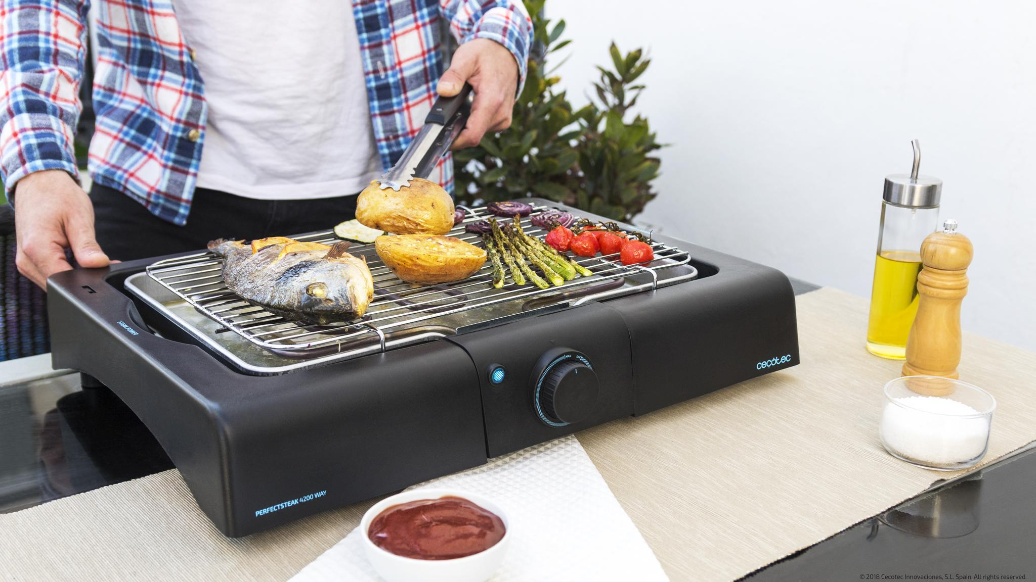 Un hombre asa pescado, patatas, espárragos y tomates en una parrilla eléctrica.