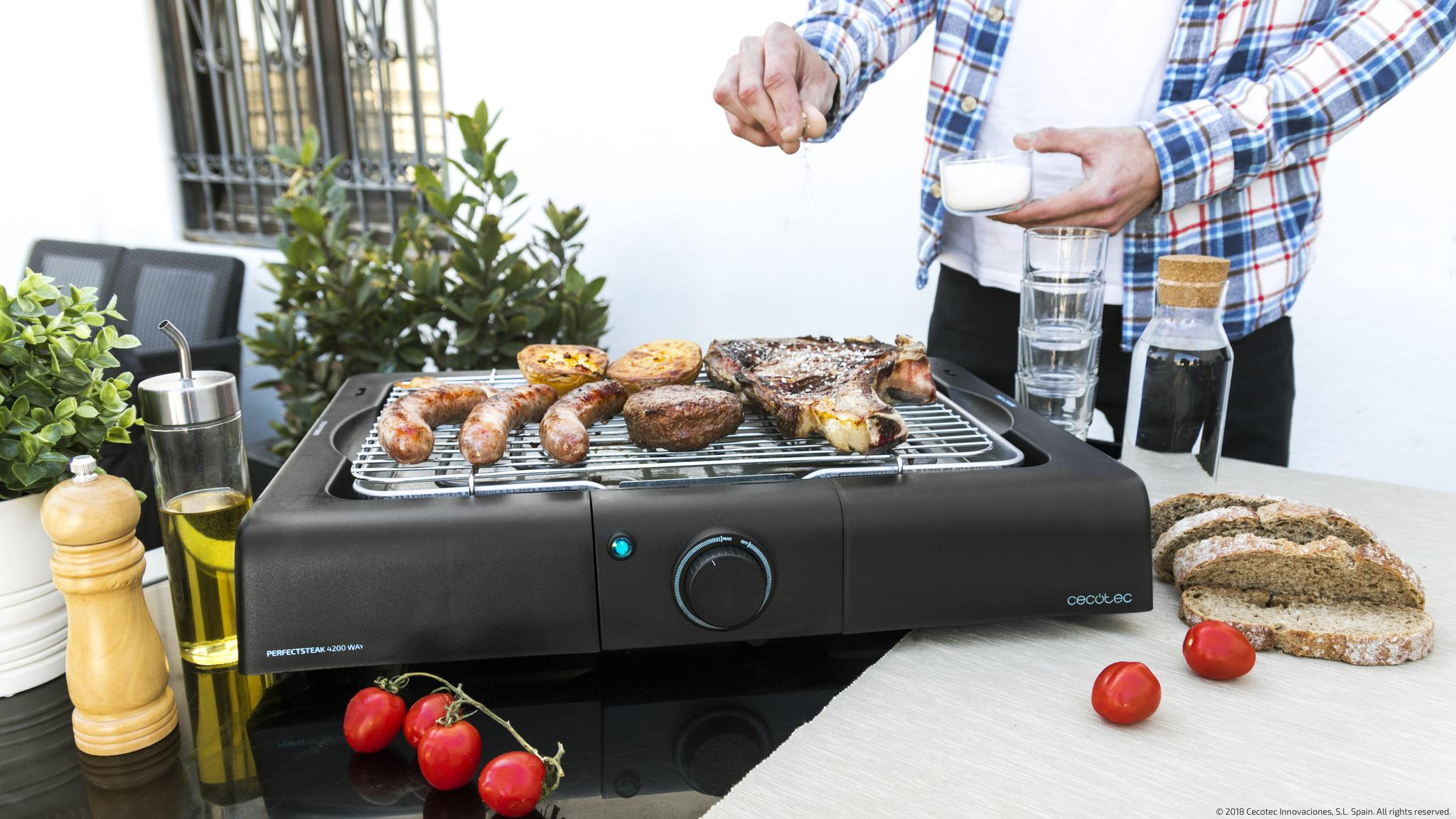 Parrilla con carne, salchichas y patatas; un hombre sazona.