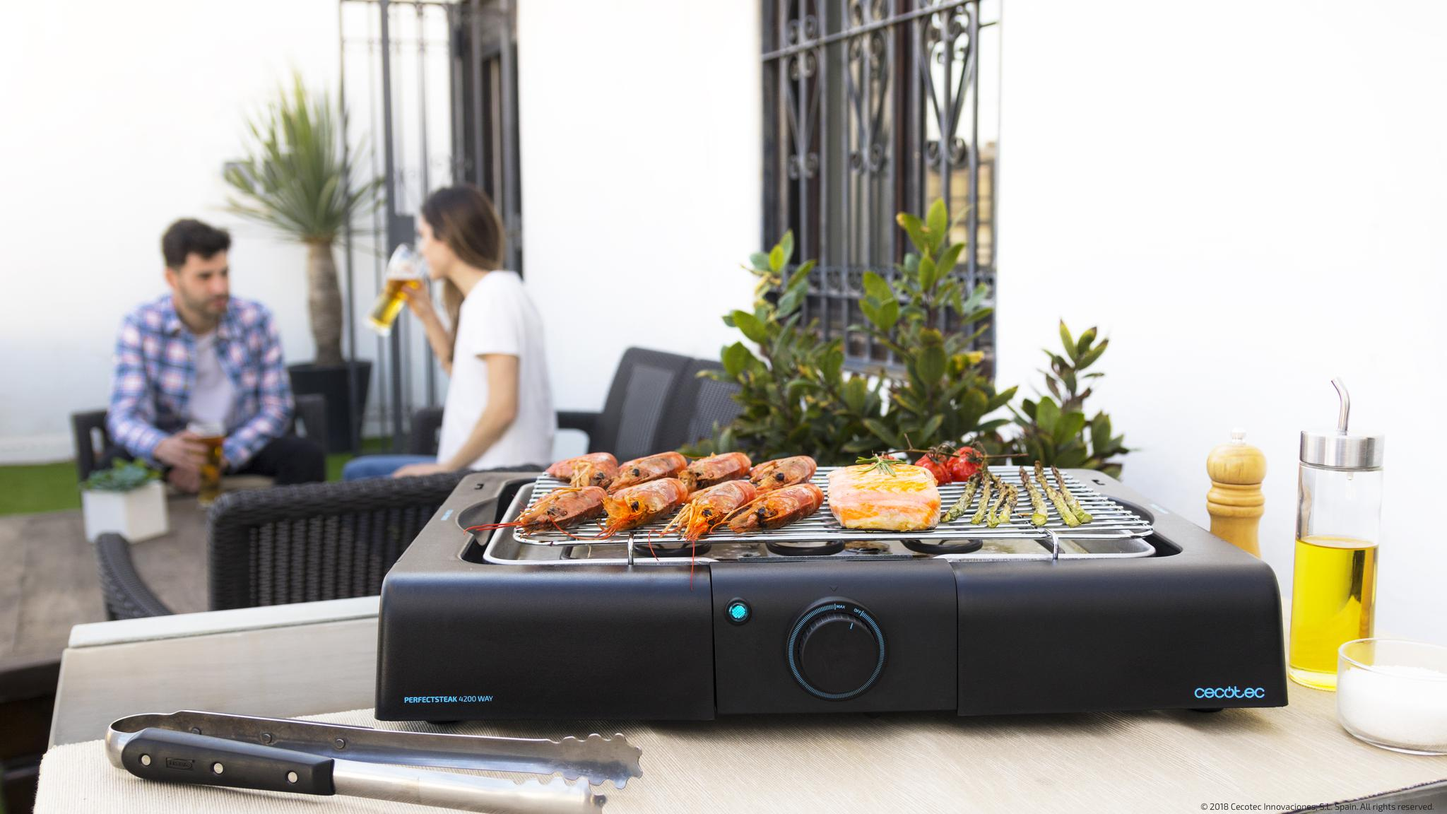 Una parrilla eléctrica negra con camarones, salmón, espárragos y tomates a la parrilla.