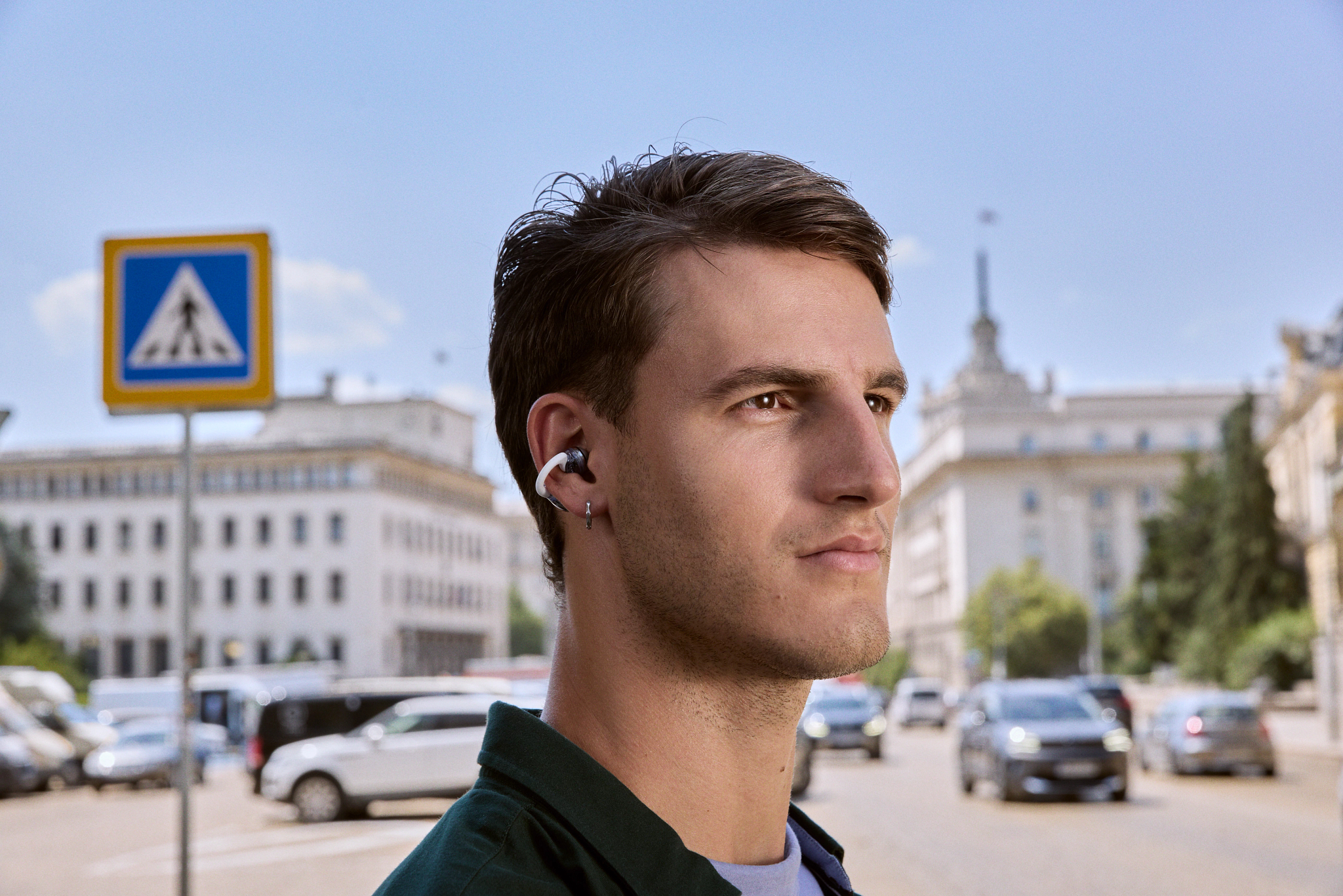 Mann mit Ohrhörern im Freien, Fußgängerzone, Autos auf der Straße im Hintergrund.
