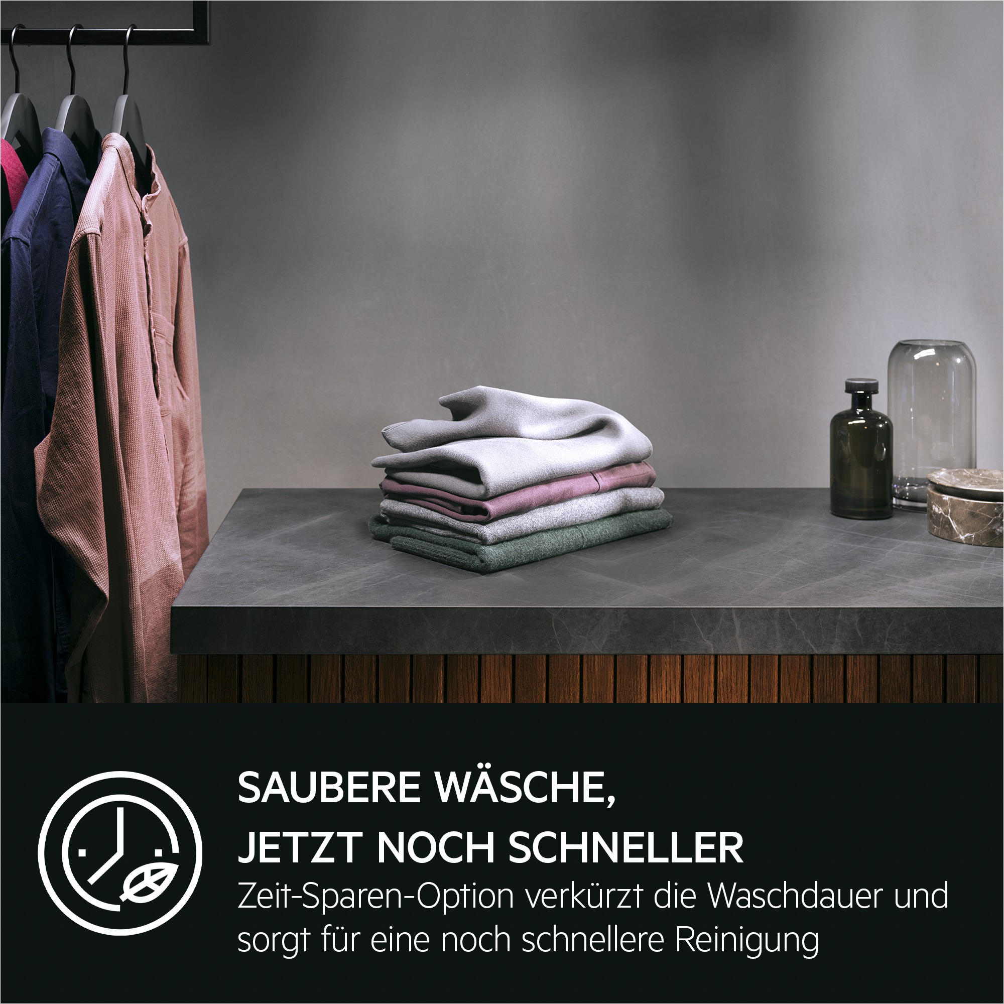 Kleidung auf Bügeln und ein Stapel gefalteter Textilien auf einer Arbeitsplatte.