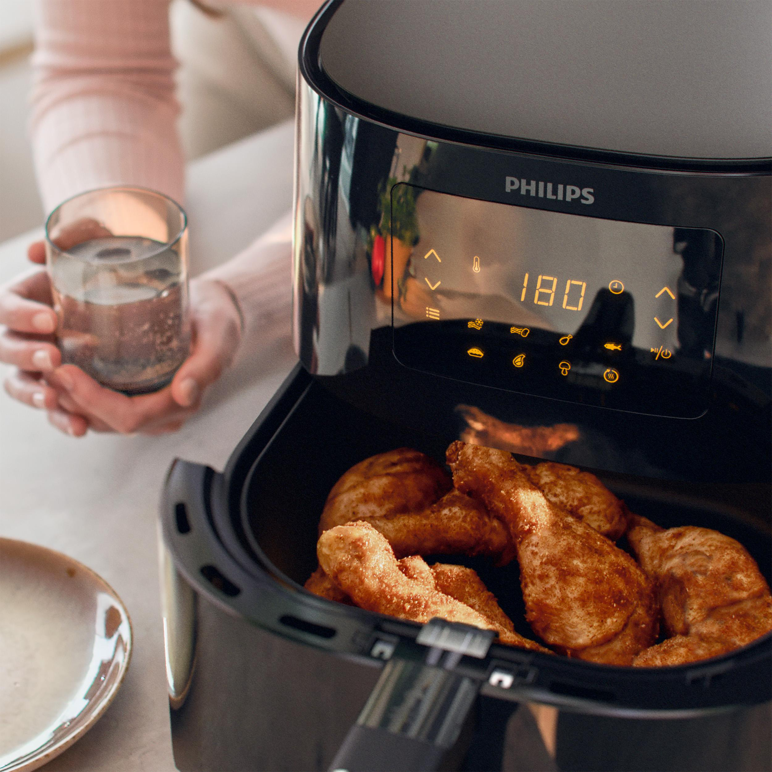 Ein Airfryer mit Hähnchenschenkeln und ein Glas Wasser.
