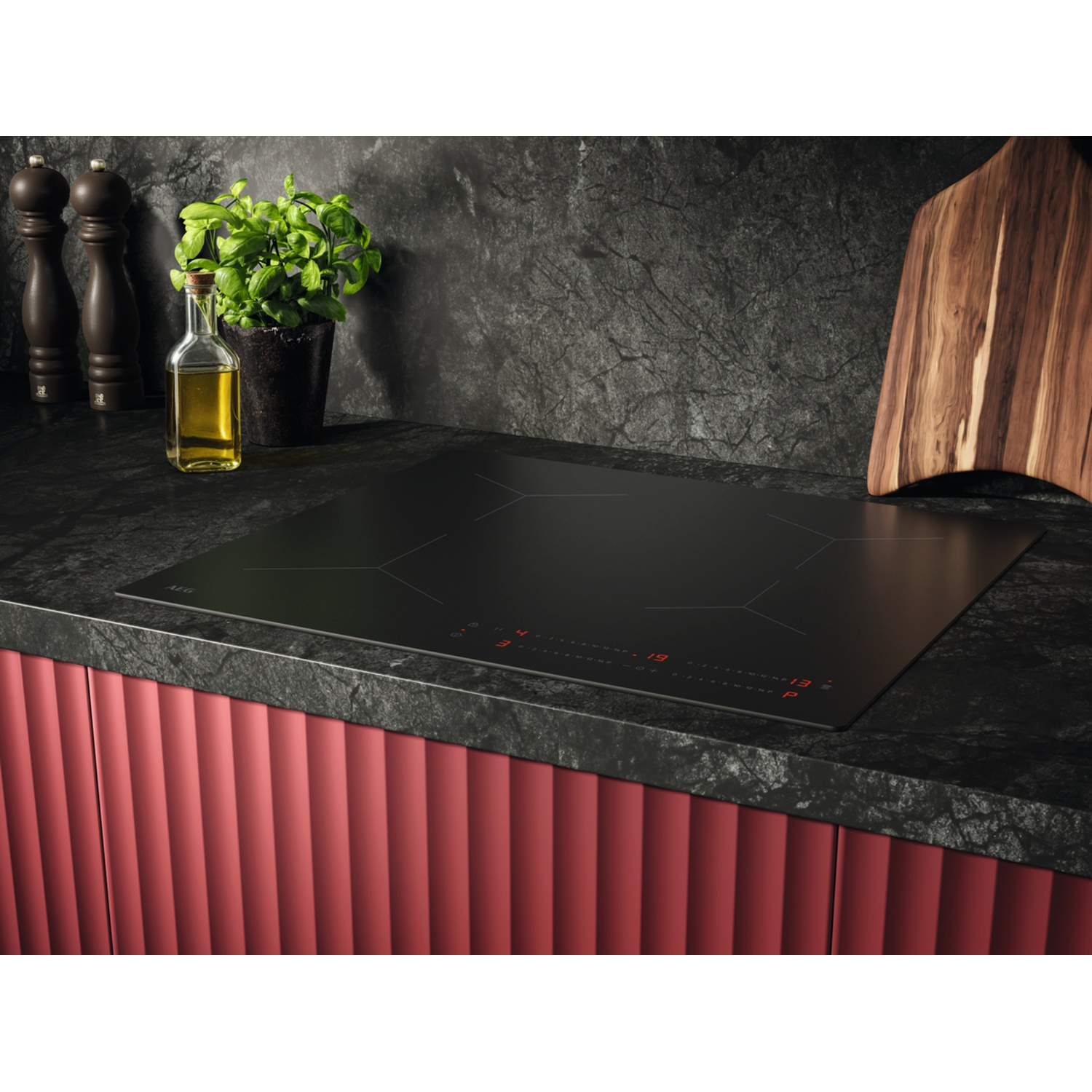 Black induction hob with red controls, next to spice mills and oil.