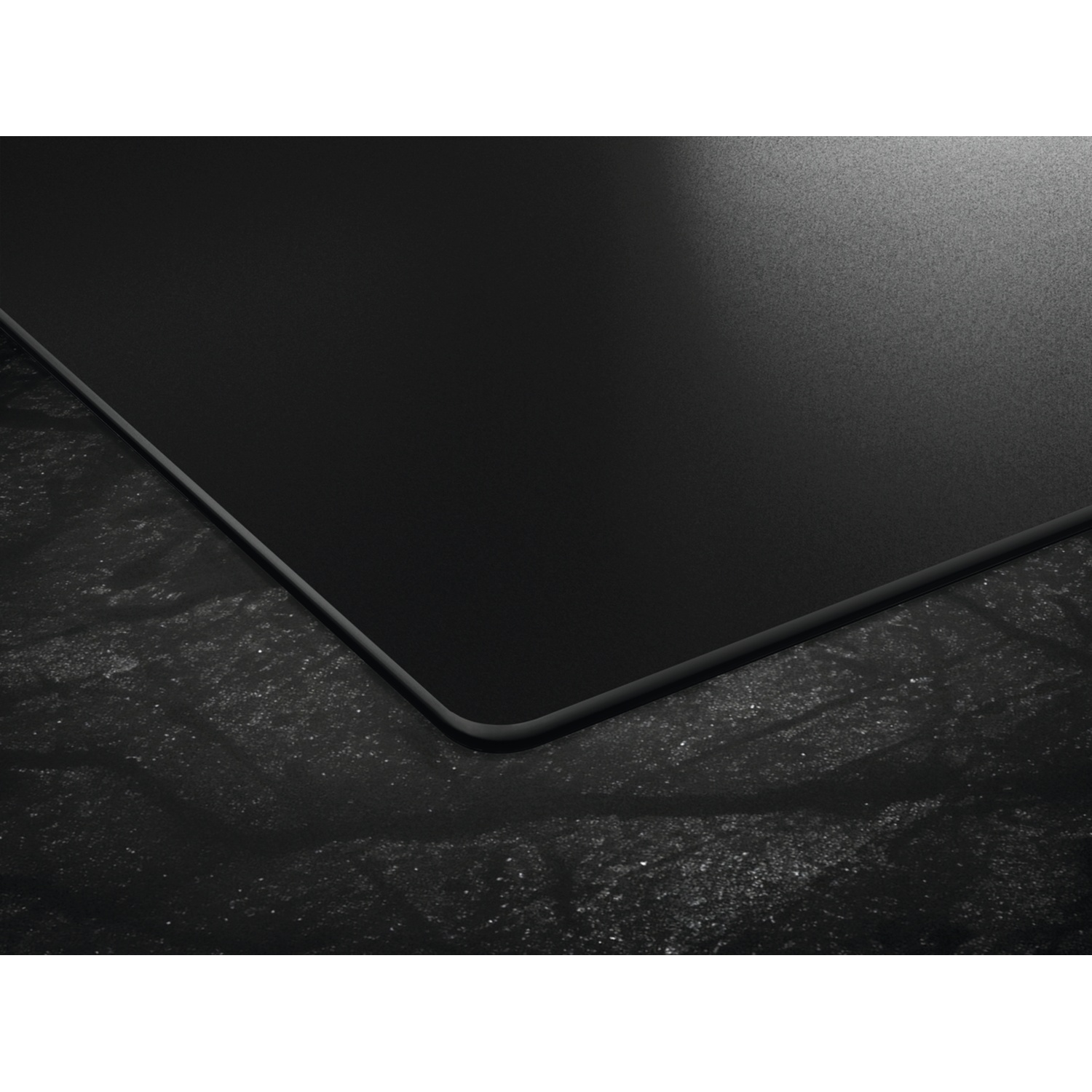 Plaque de cuisson noire aux coins arrondis sur fond sombre.