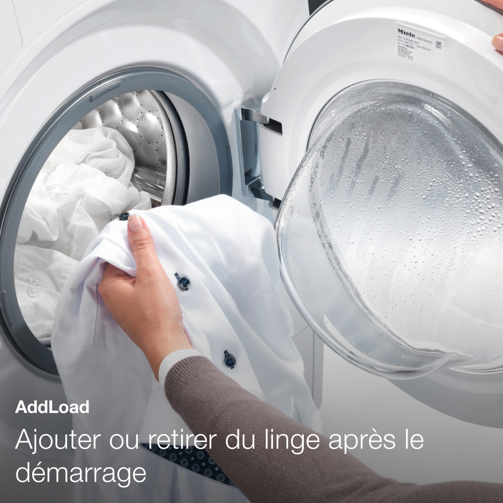 Une main place une chemise blanche dans une machine à laver ouverte avec du linge.