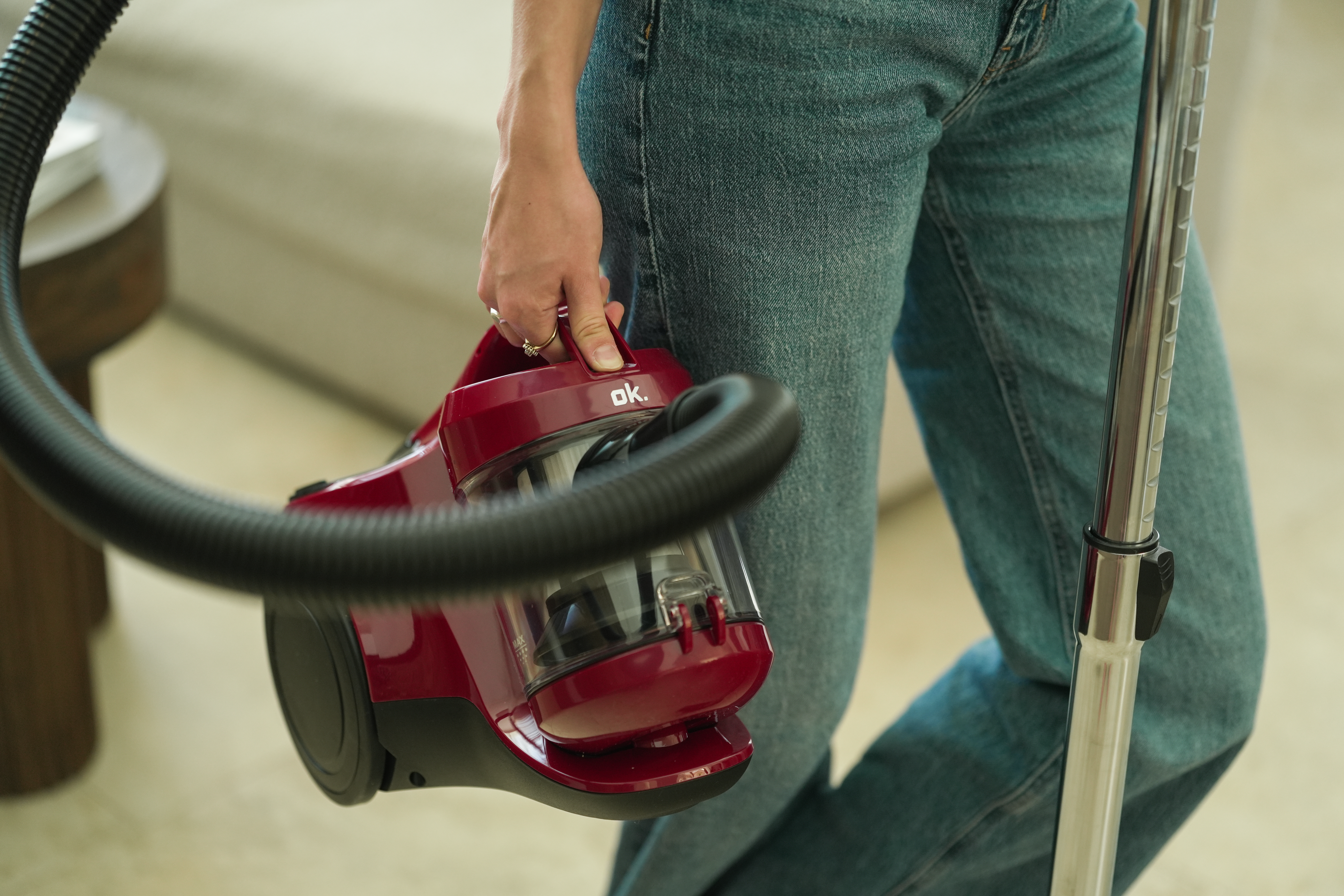 Osoba w dżinsach trzymająca czerwony odkurzacz z wężem i rurą.