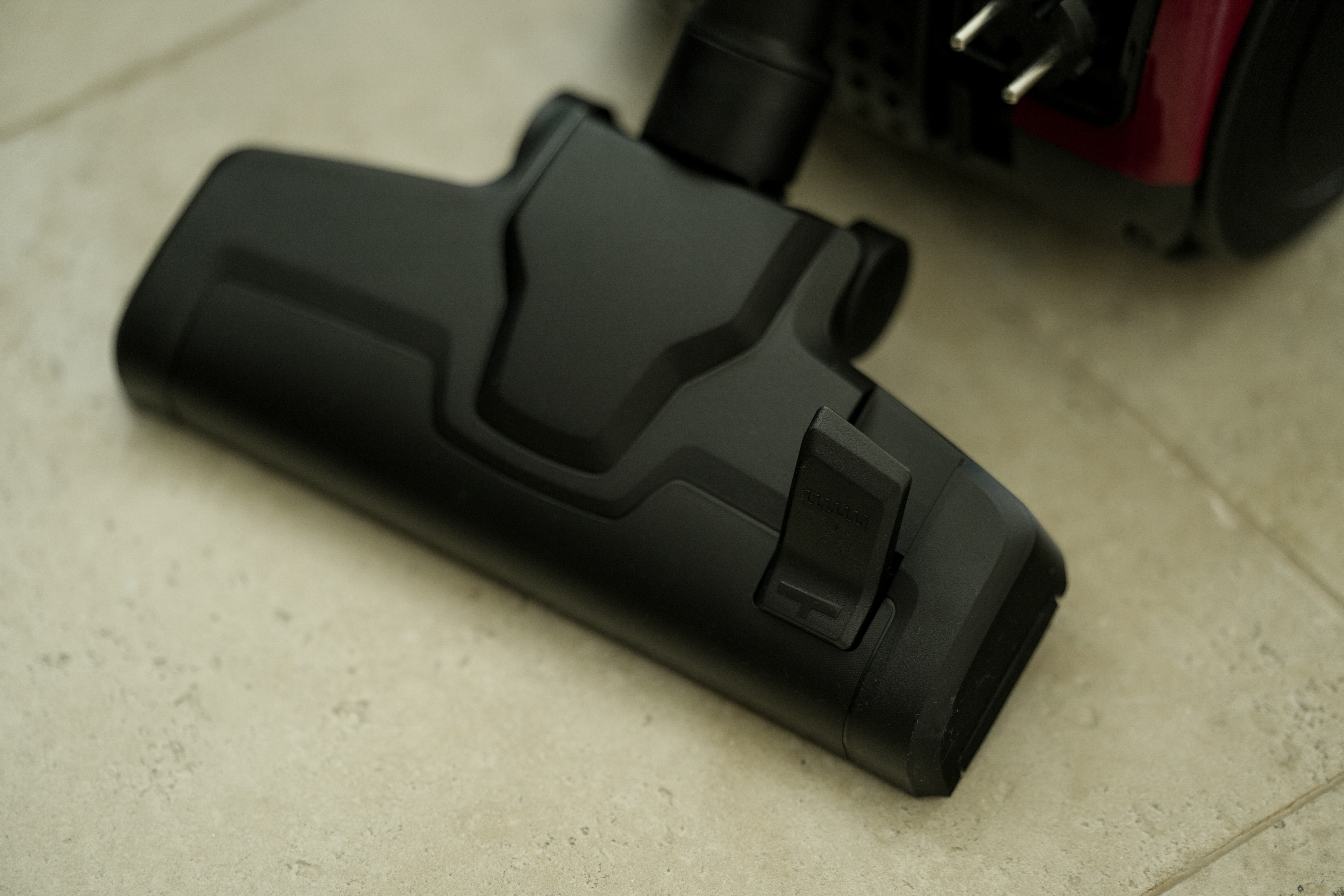 Czarna głowica odkurzacza z zatrzaskiem na jasnej podłodze.