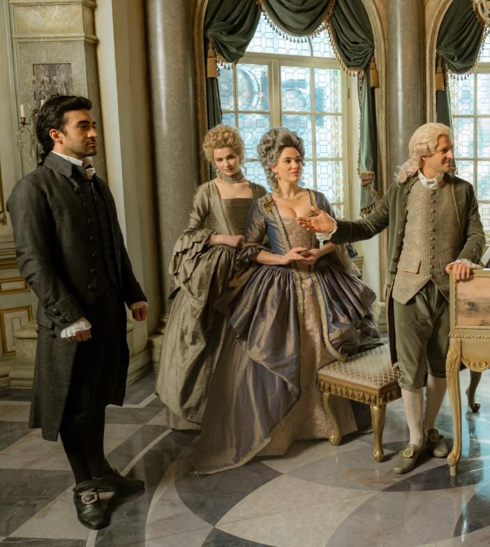 Vier Personen in historischer Kleidung stehen in einem opulenten Raum mit großen Fenstern.