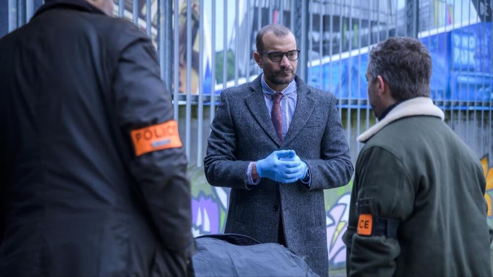 Polizisten in blauer Handschuhe und Mänteln stehen vor einer Absperrung.