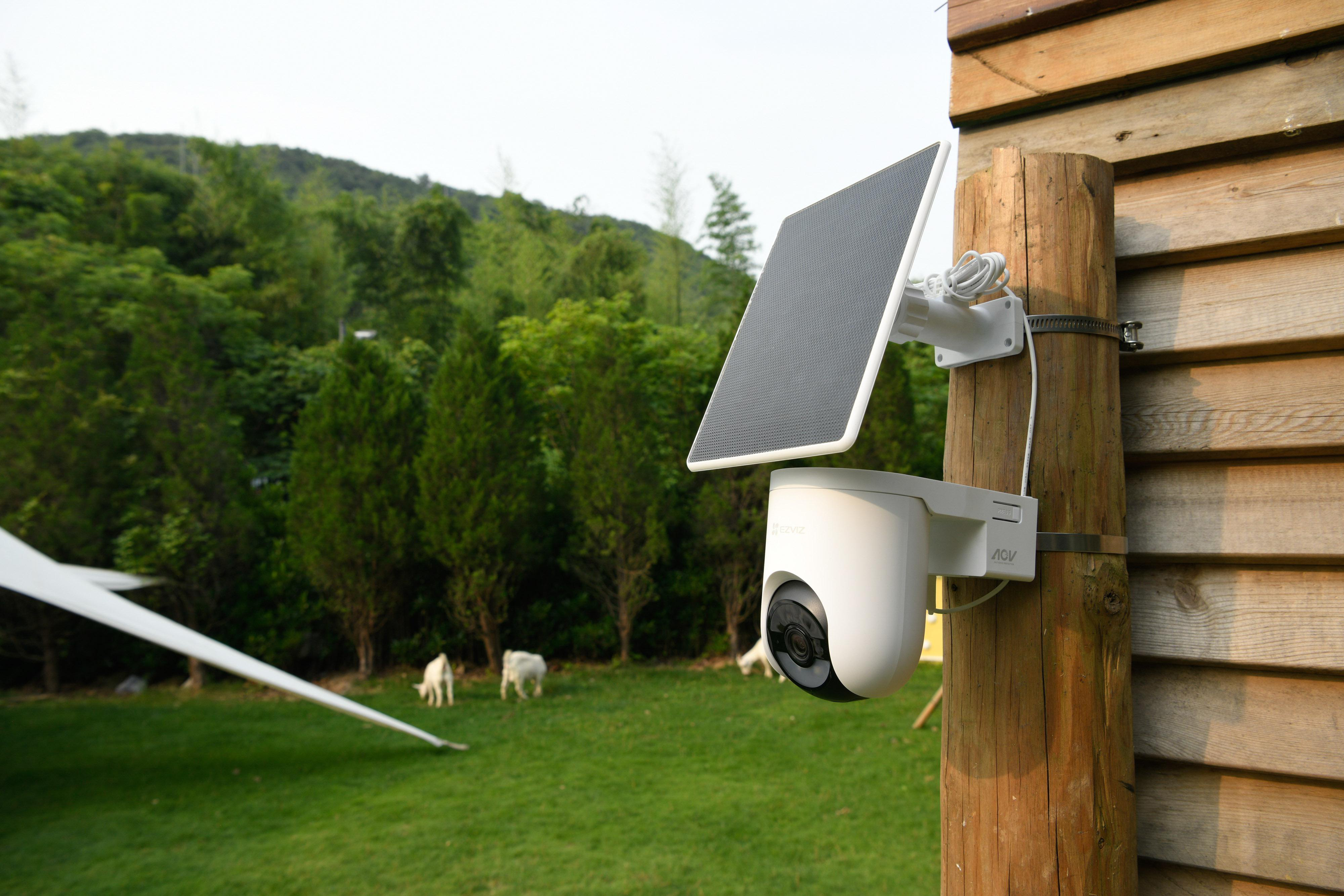 Eine weiße Überwachungskamera mit Solarpanel ist an einem Holzpfosten befestigt.