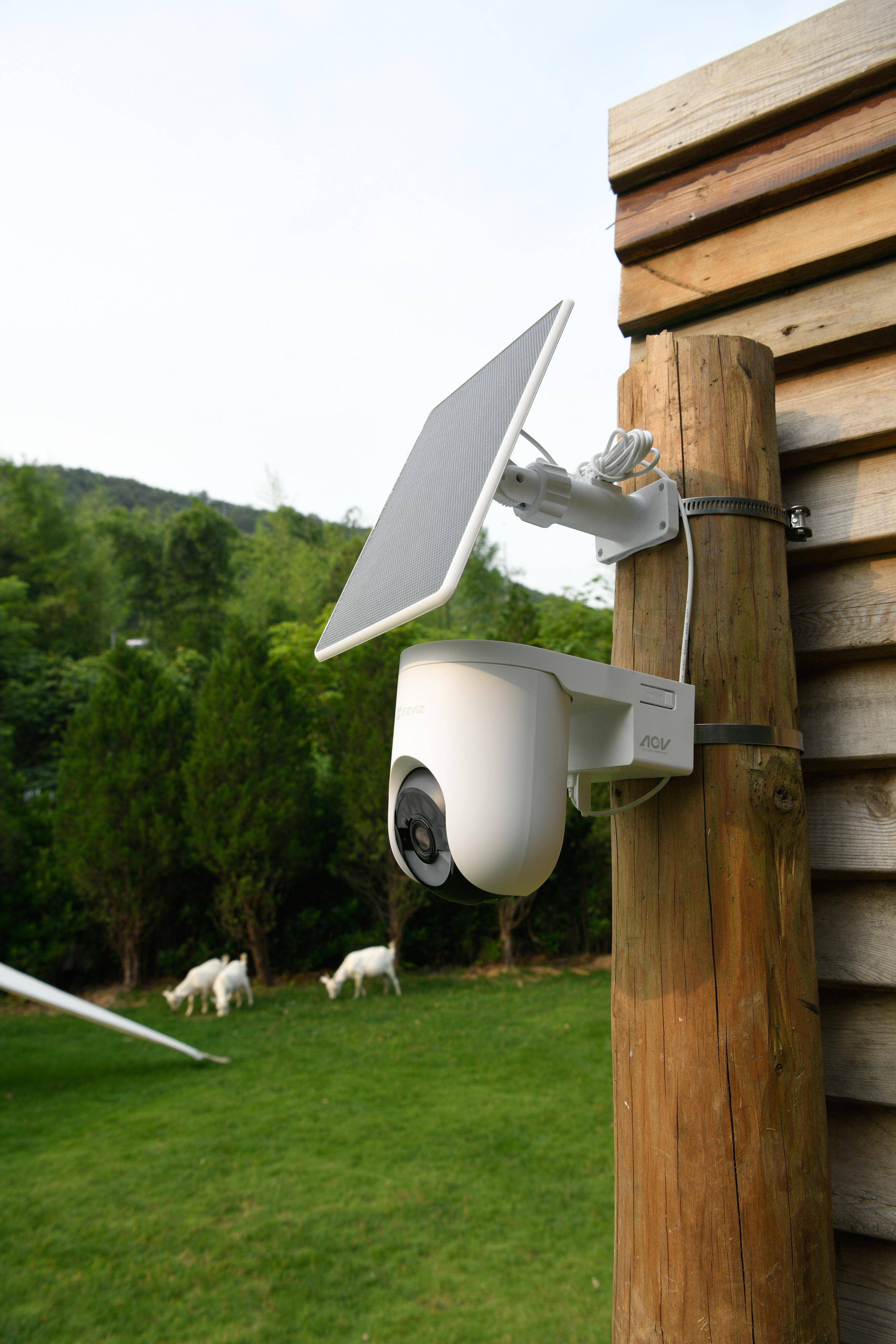 Eine weiße Überwachungskamera mit Solarpanel ist an einem Holzpfosten montiert.