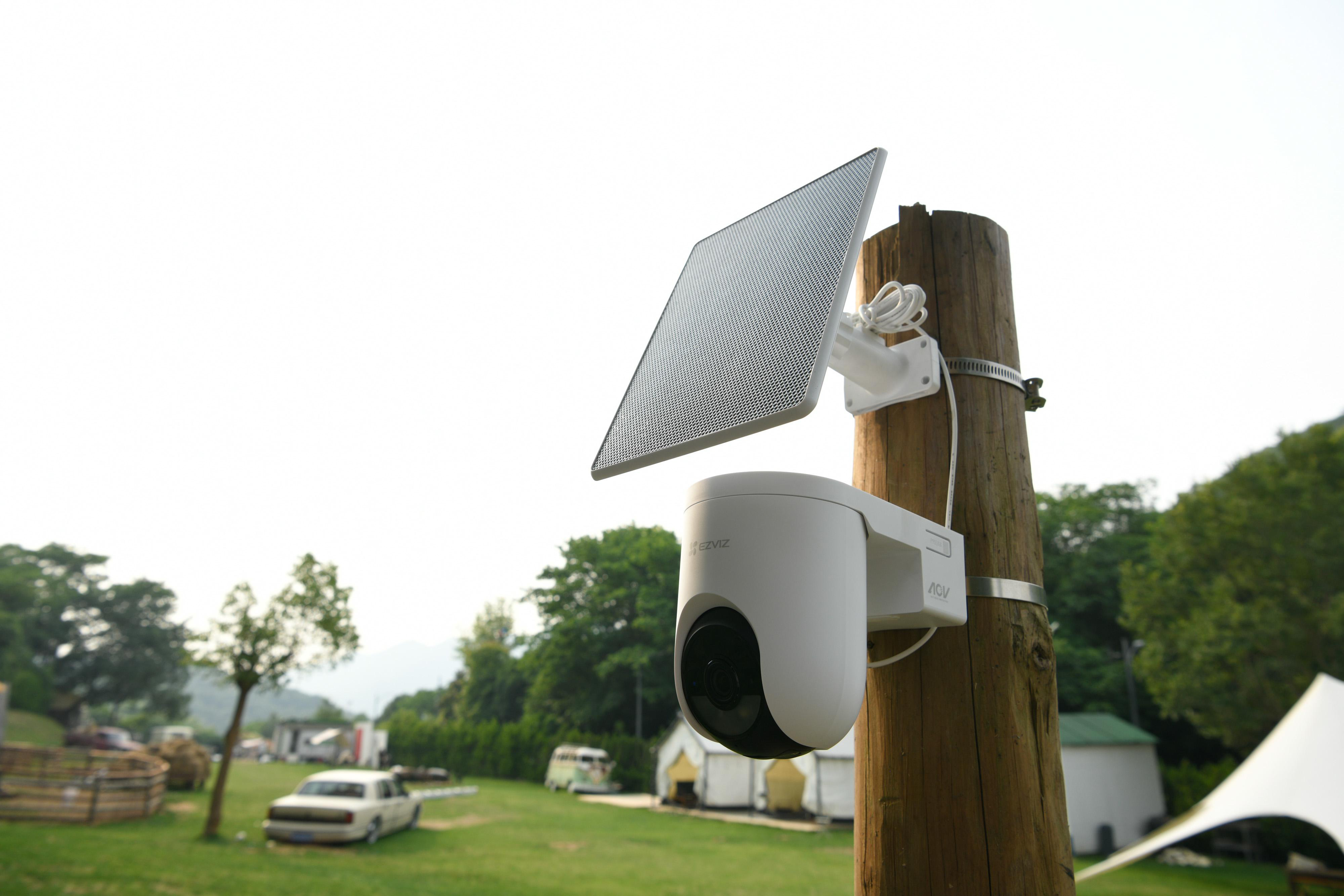 Eine weiße Überwachungskamera mit Solarpanel ist an einem Holzpfahl befestigt.