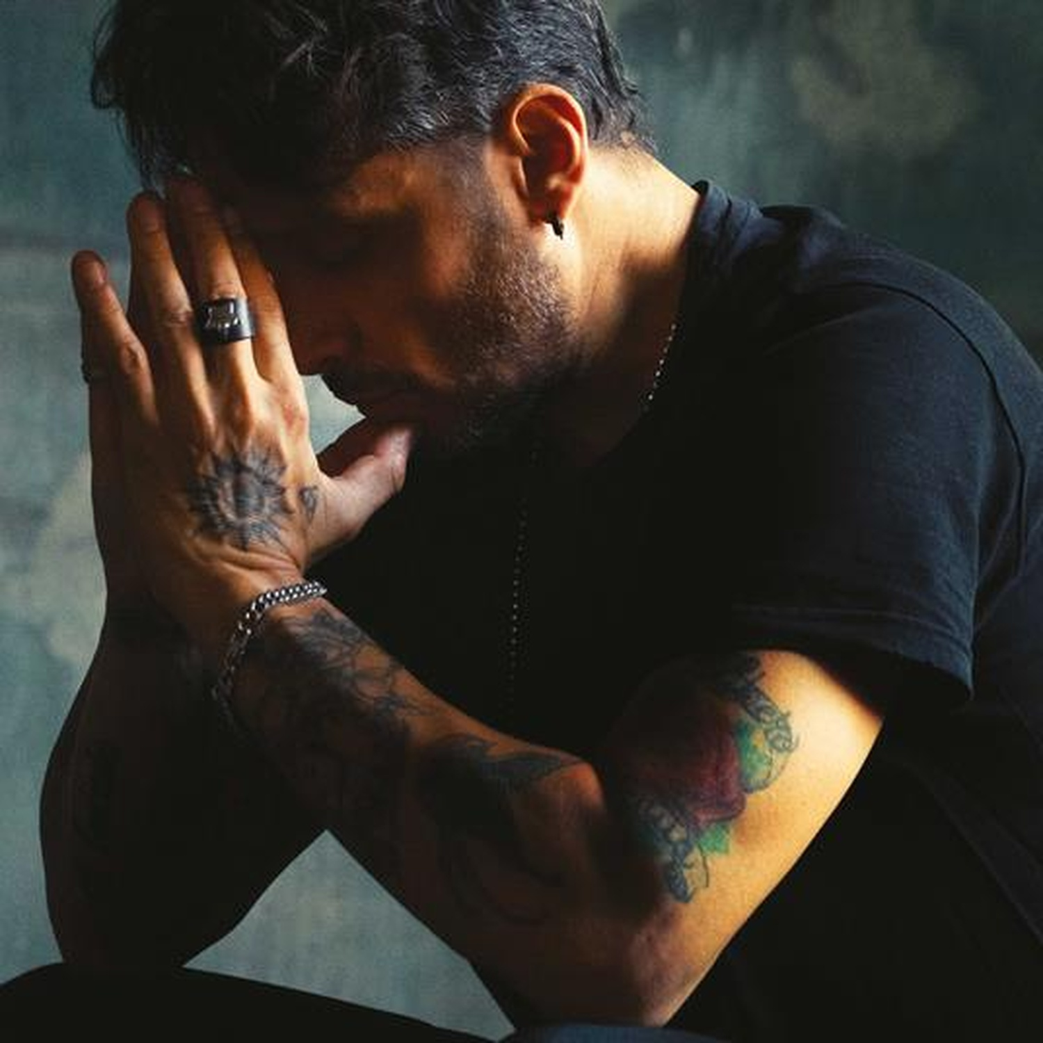 Un uomo con le braccia tatuate, mani giunte davanti al viso.