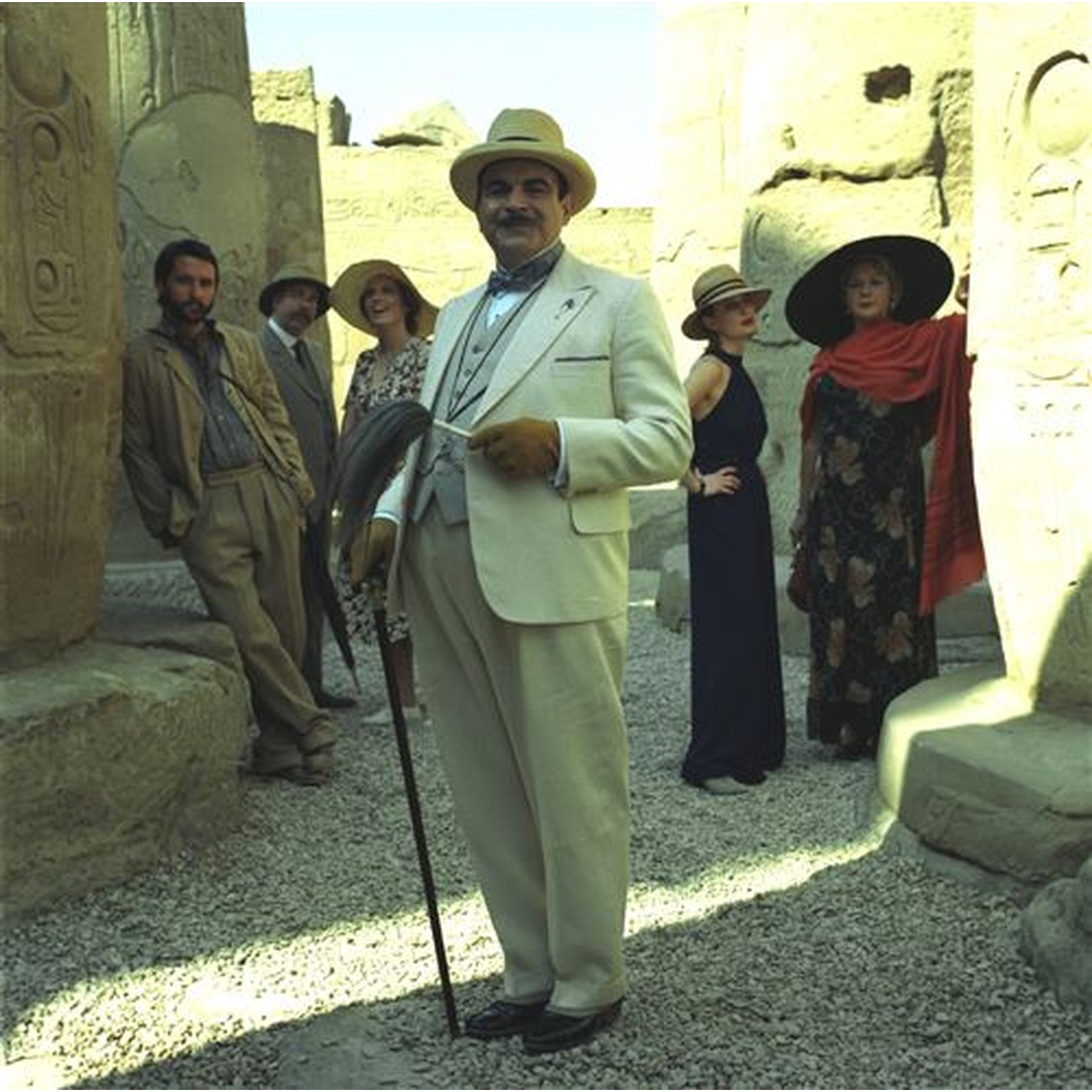 Un groupe de personnes en tenue du début du XXe siècle se tient entre des piliers antiques.