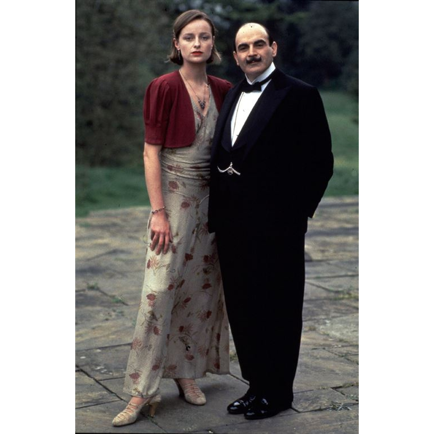 Homme en smoking et femme en robe et veste rouge dehors.