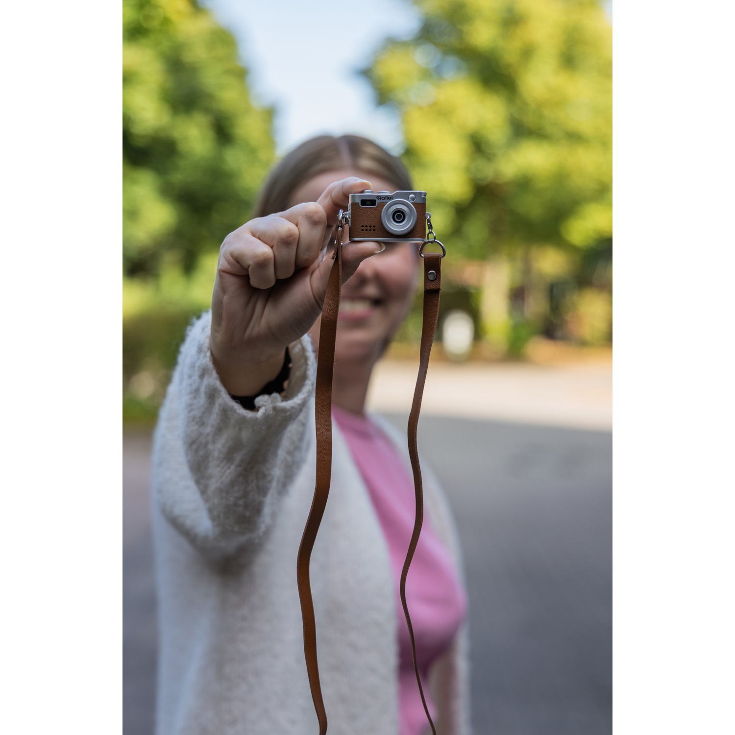 Vrouw houdt kleine bruine camera vast, draagt witte vest, roze top.