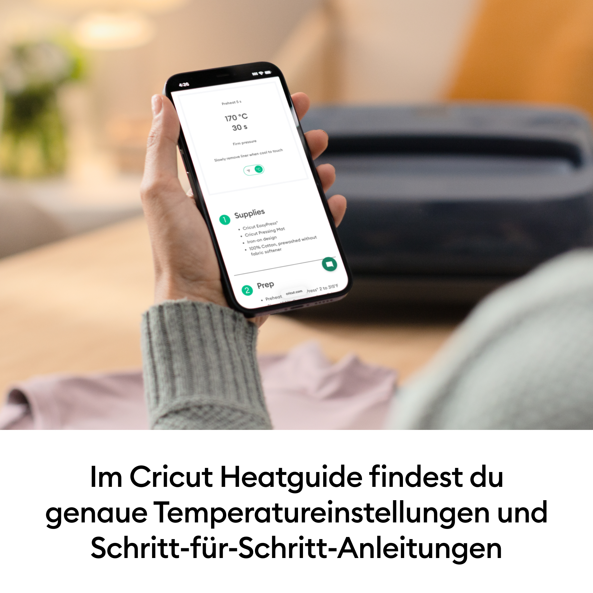 Eine Hand hält ein Smartphone mit der Cricut Heatguide App, die Anleitungen anzeigt.
