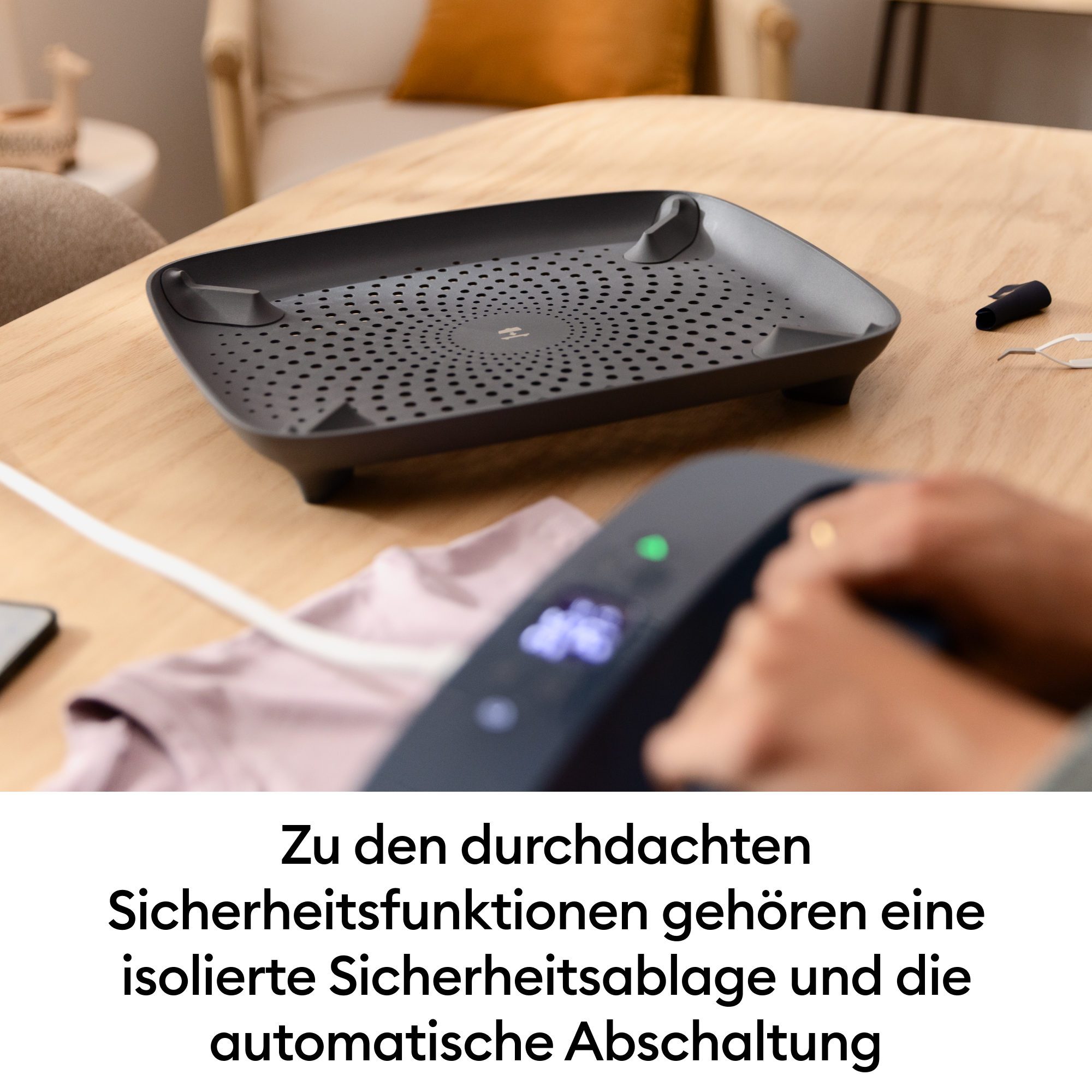 Ein Bügeleisen ruht auf einem Kleiderstück, daneben eine graue Ablage.