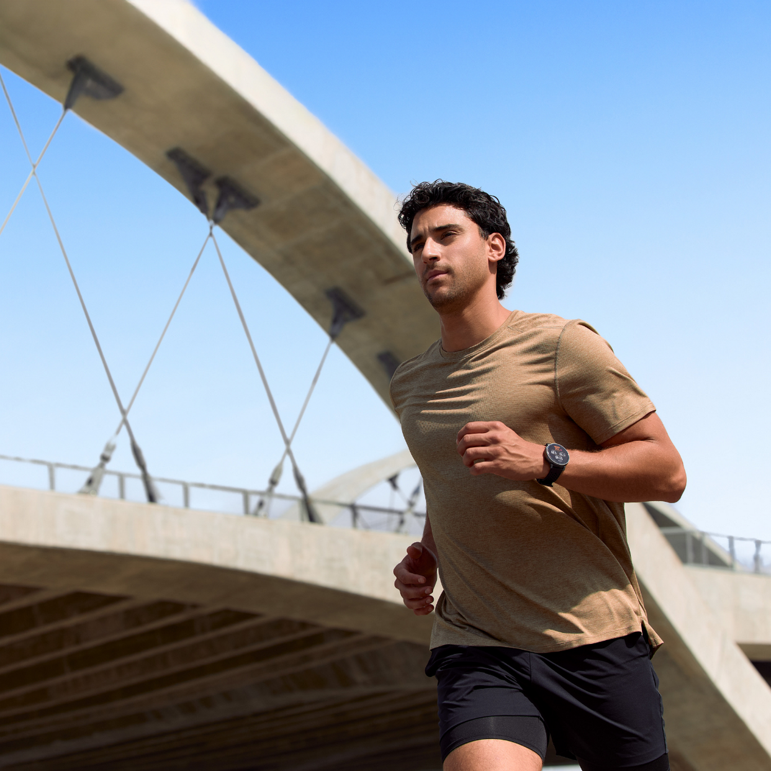 Un hombre corre al aire libre bajo un puente con cielo azul.