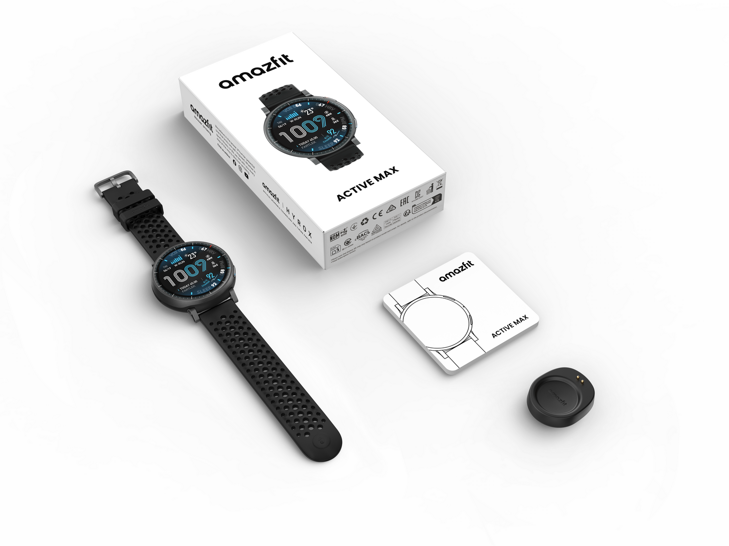 Un smartwatch Amazfit Active Max negro, su caja, una pequeña tarjeta y un cargador están ordenadamente dispuestos sobre una superficie blanca.