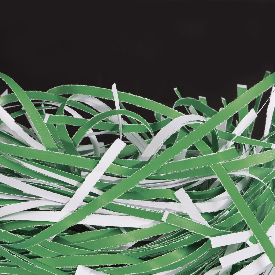 Grüne und weiße Papierschnipsel liegen übereinander auf schwarzem Hintergrund.