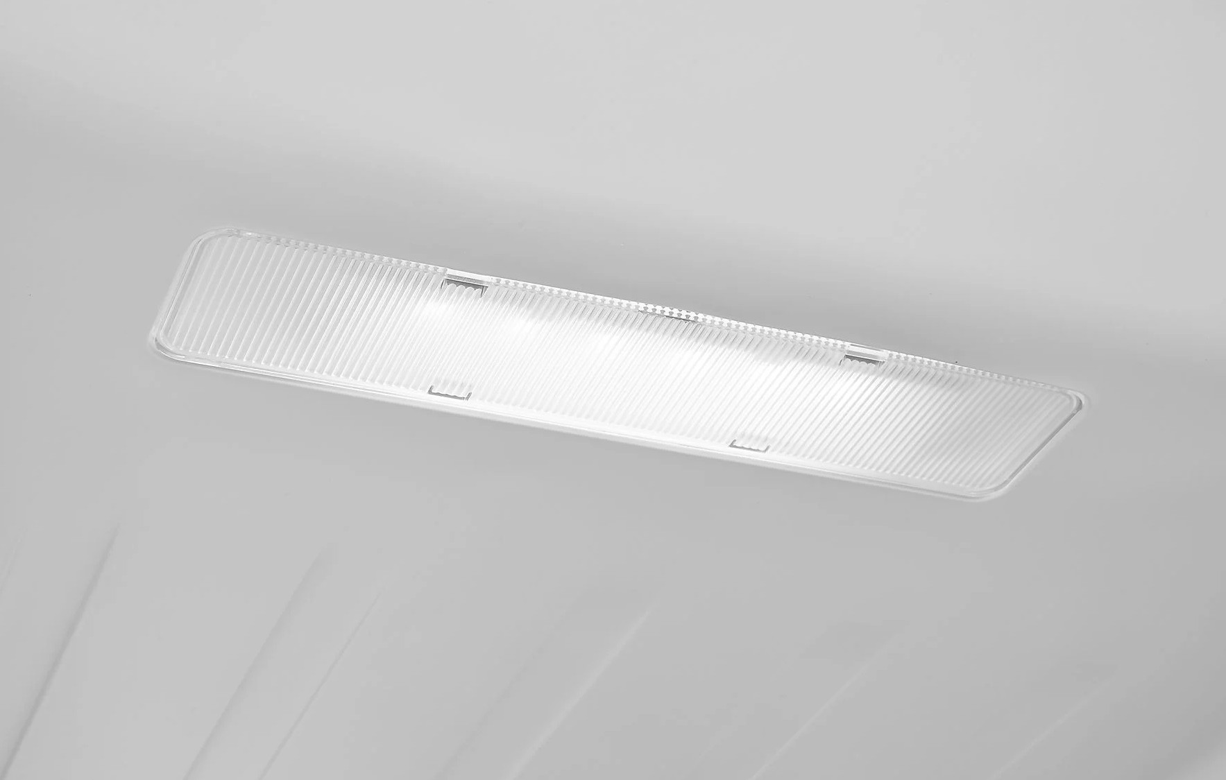 Białe wnętrze lodówki z przezroczystą osłoną światła.