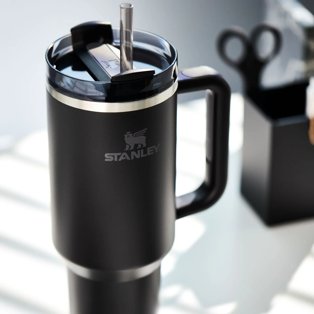 Siyah kulp ve pipetli bardak, önünde Stanley logosu bulunur.