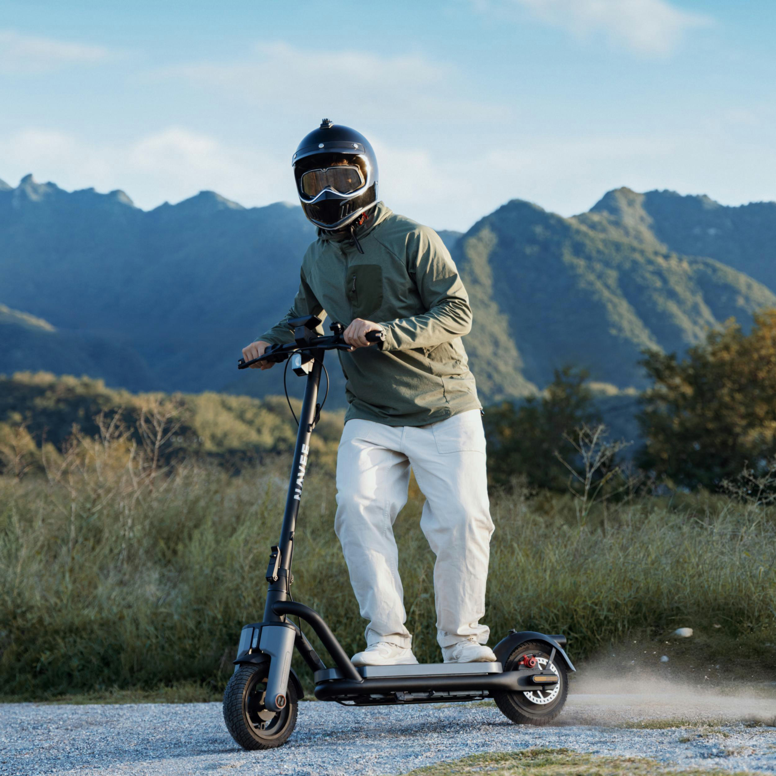 Mann fährt Elektroroller in bergiger Landschaft, Staub wirbelt auf.