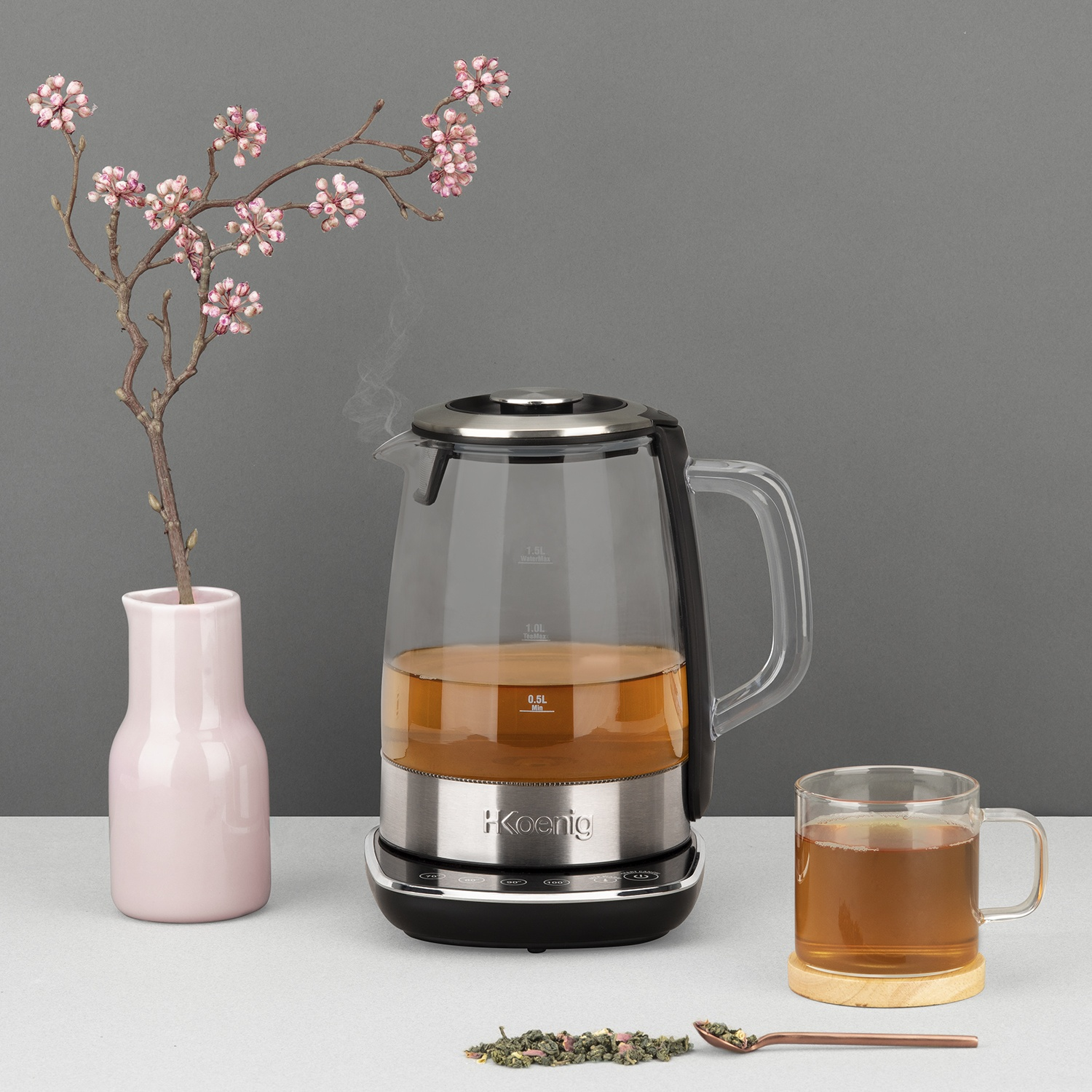 Un bollitore in vetro con tè, una tazza di tè, un vaso con fiori e un cucchiaio.