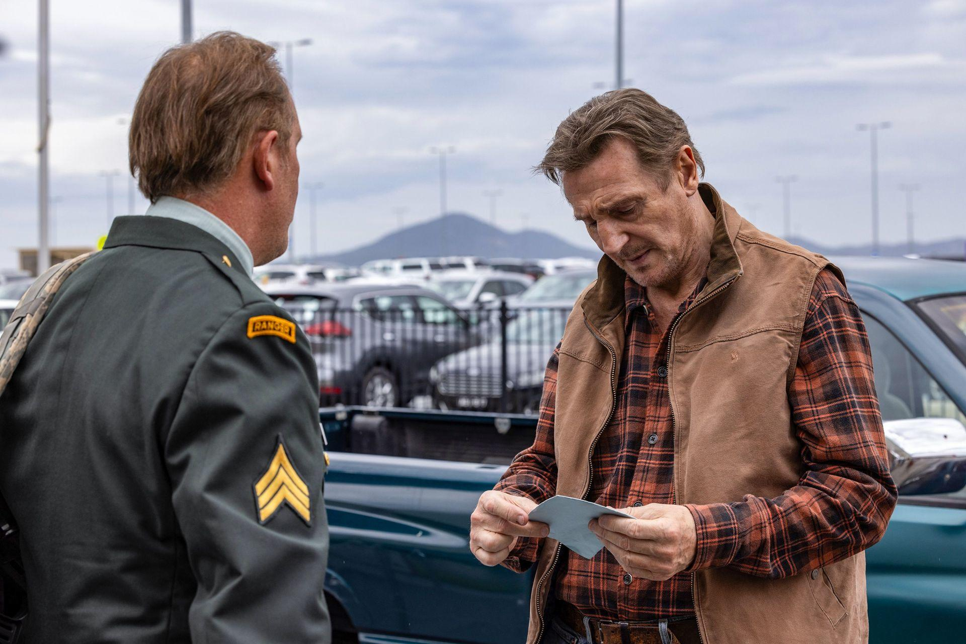 Ein Ranger in Uniform spricht mit einem Mann in Weste und kariertem Hemd.