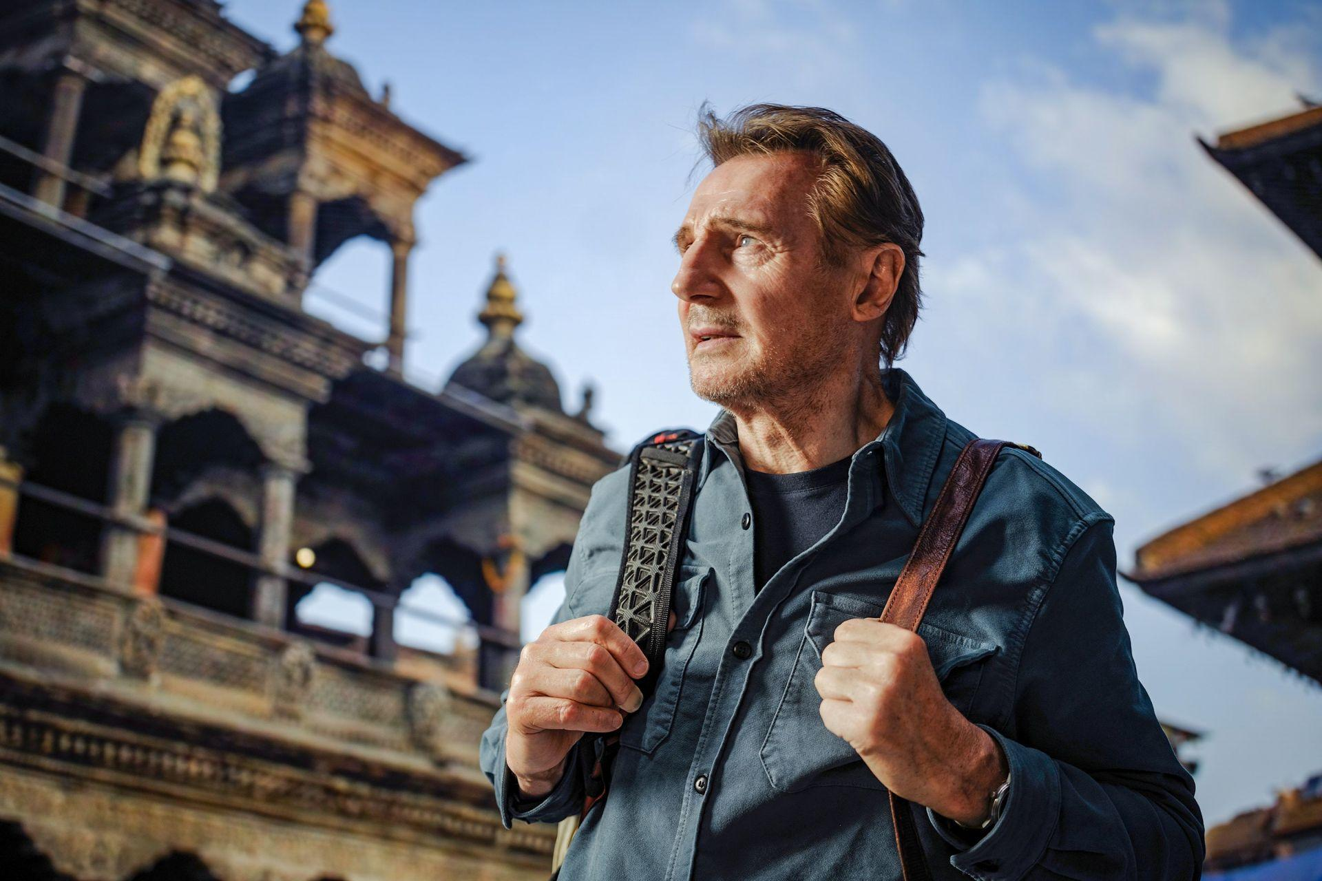 Ein Mann mit Rucksack steht vor einem Tempel im Freien.
