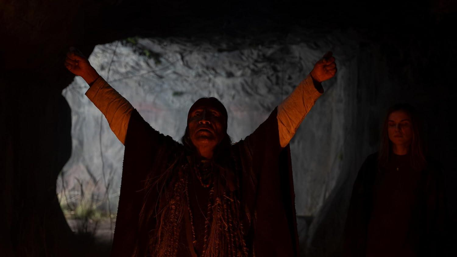 Ein Mann mit erhobenen Armen und eine Frau mit geschlossenen Augen in dunkler Höhle.