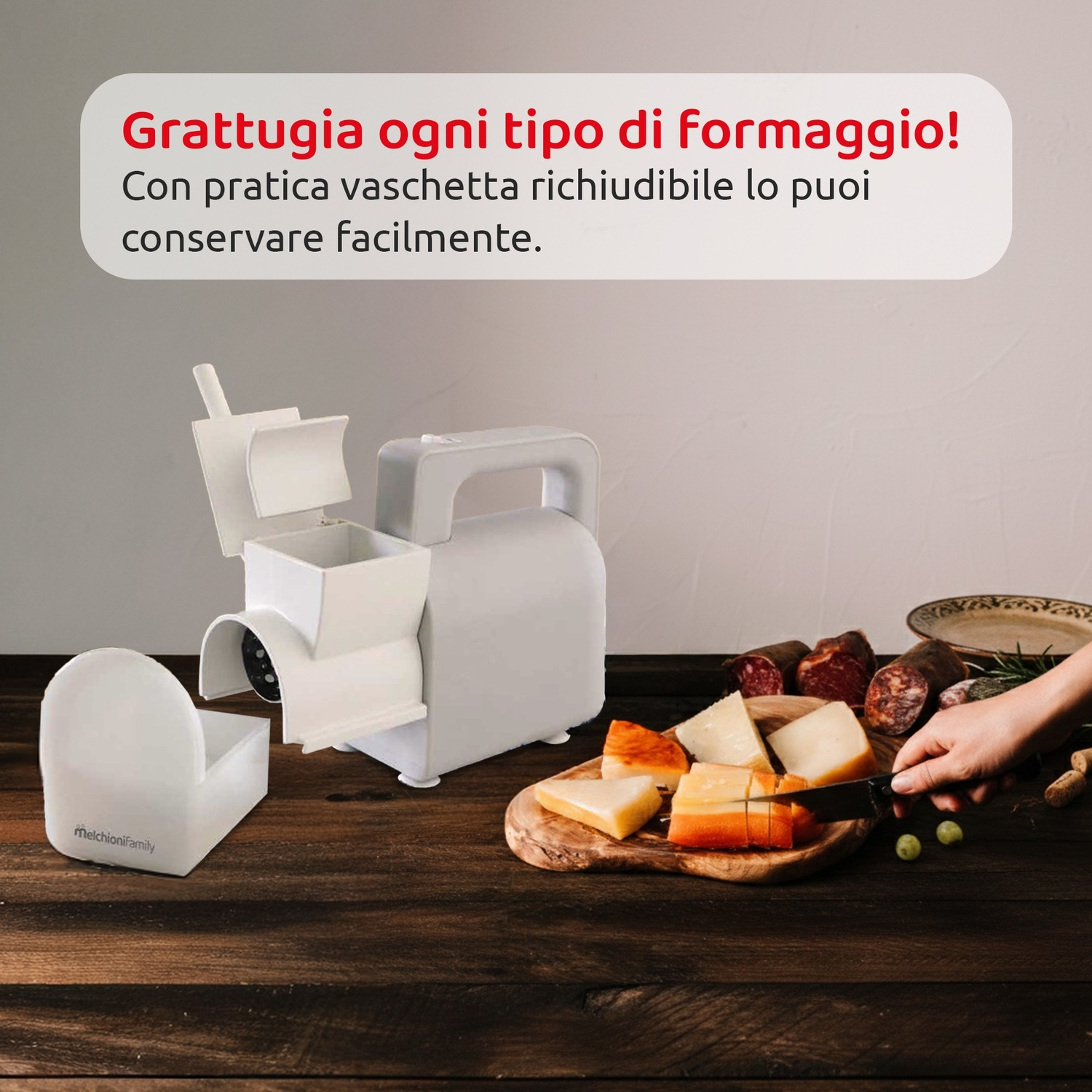 Una grattugia bianca con contenitore sta su un tavolo di legno vicino a formaggio e salumi.