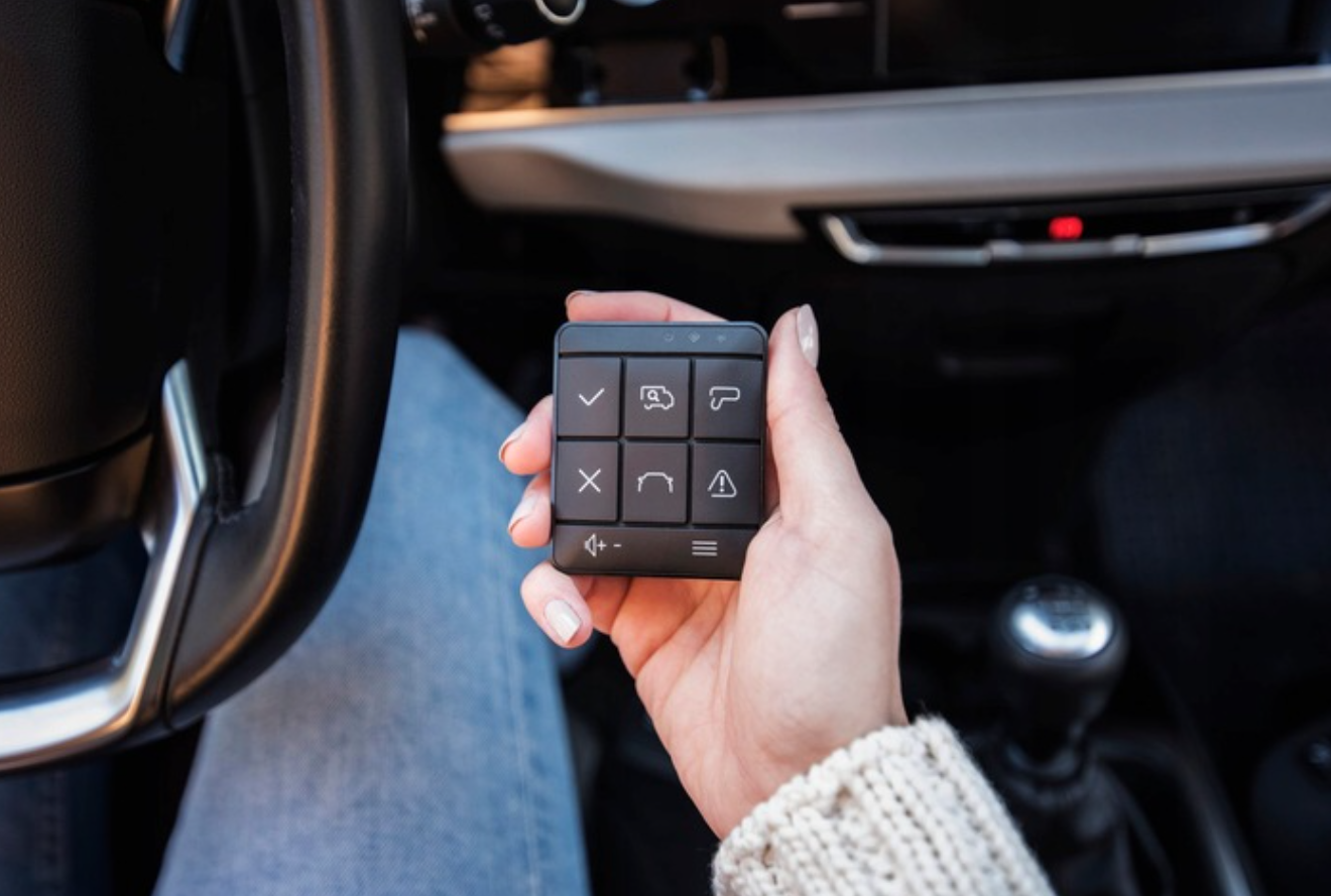 Dłoń trzyma czarny panel sterowania z ikonami w samochodzie.