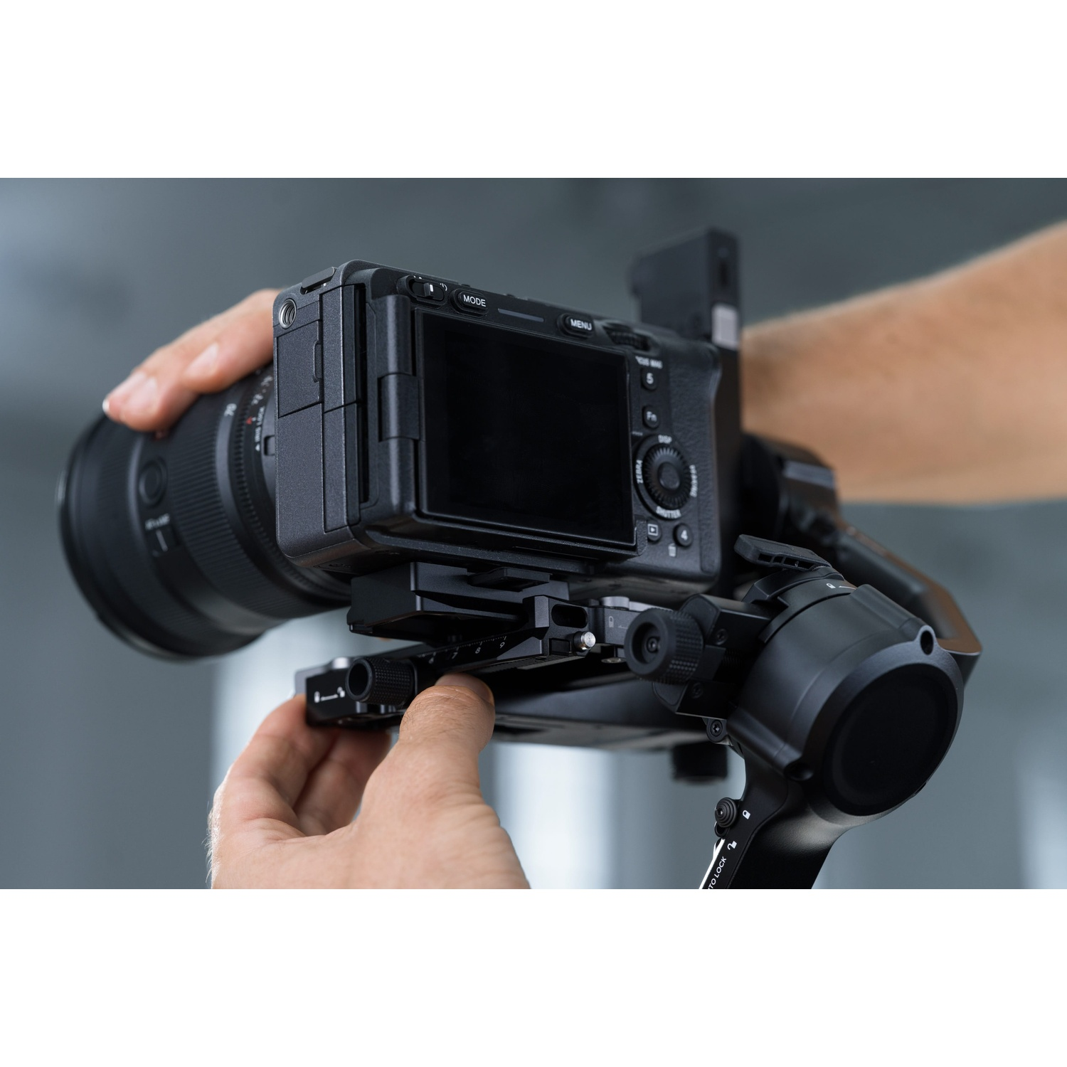 Mains ajustant une caméra sur un stabilisateur, focalisant sur l'objectif et les commandes.
