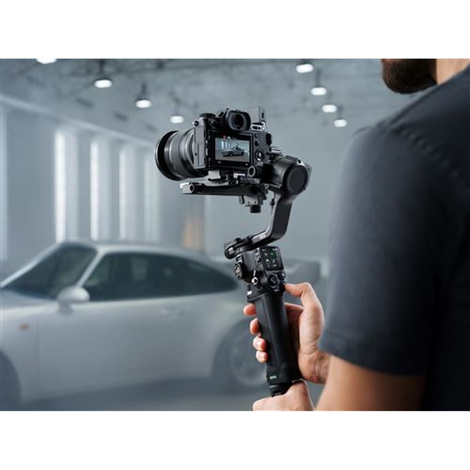 A man holds a camera gimbal. A white car is in the background.