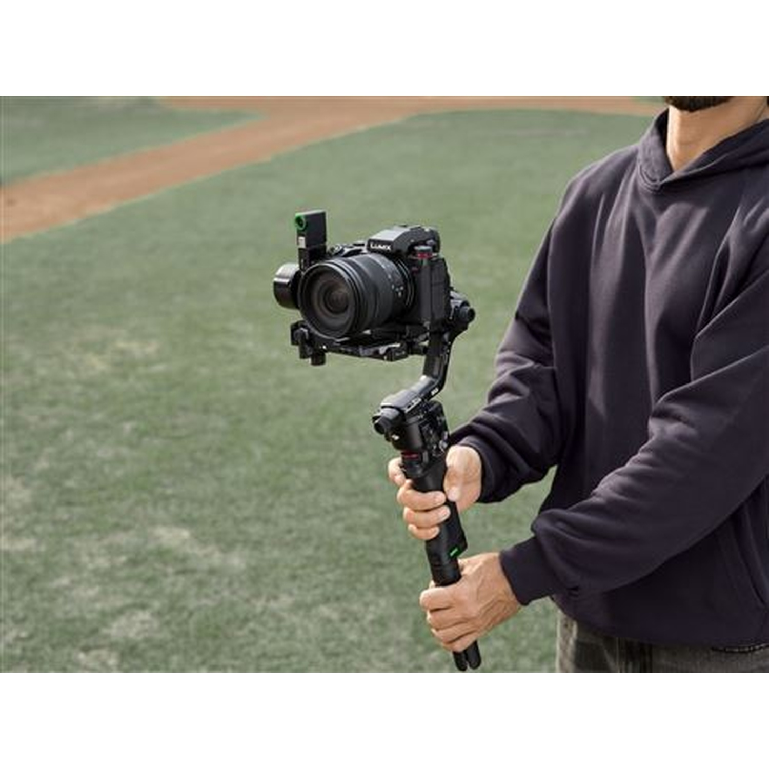 A person holds a camera gimbal on a sports field.